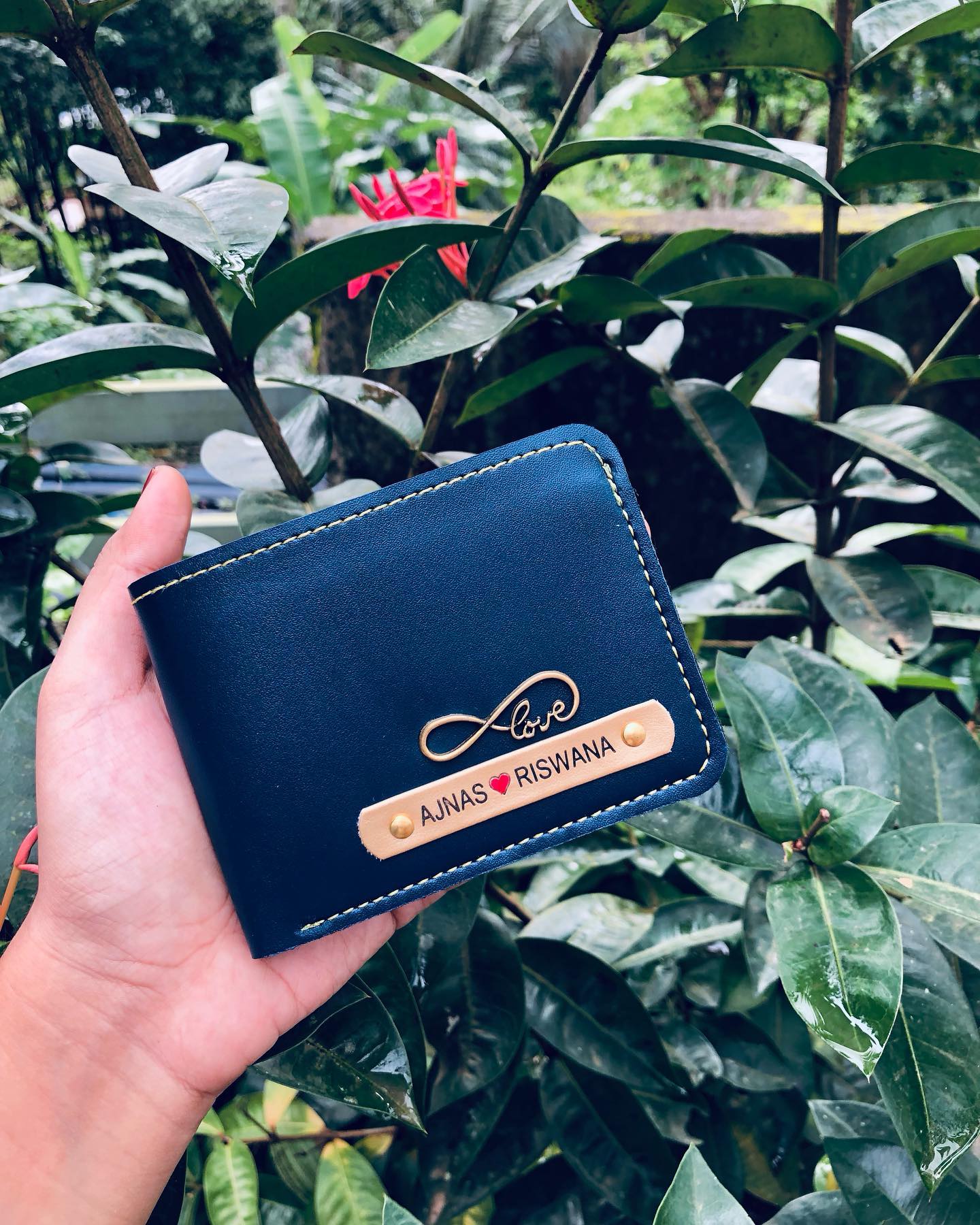 A navy leather wallet engraved with an infinity love symbol and a couple's names on a tan nameplate.