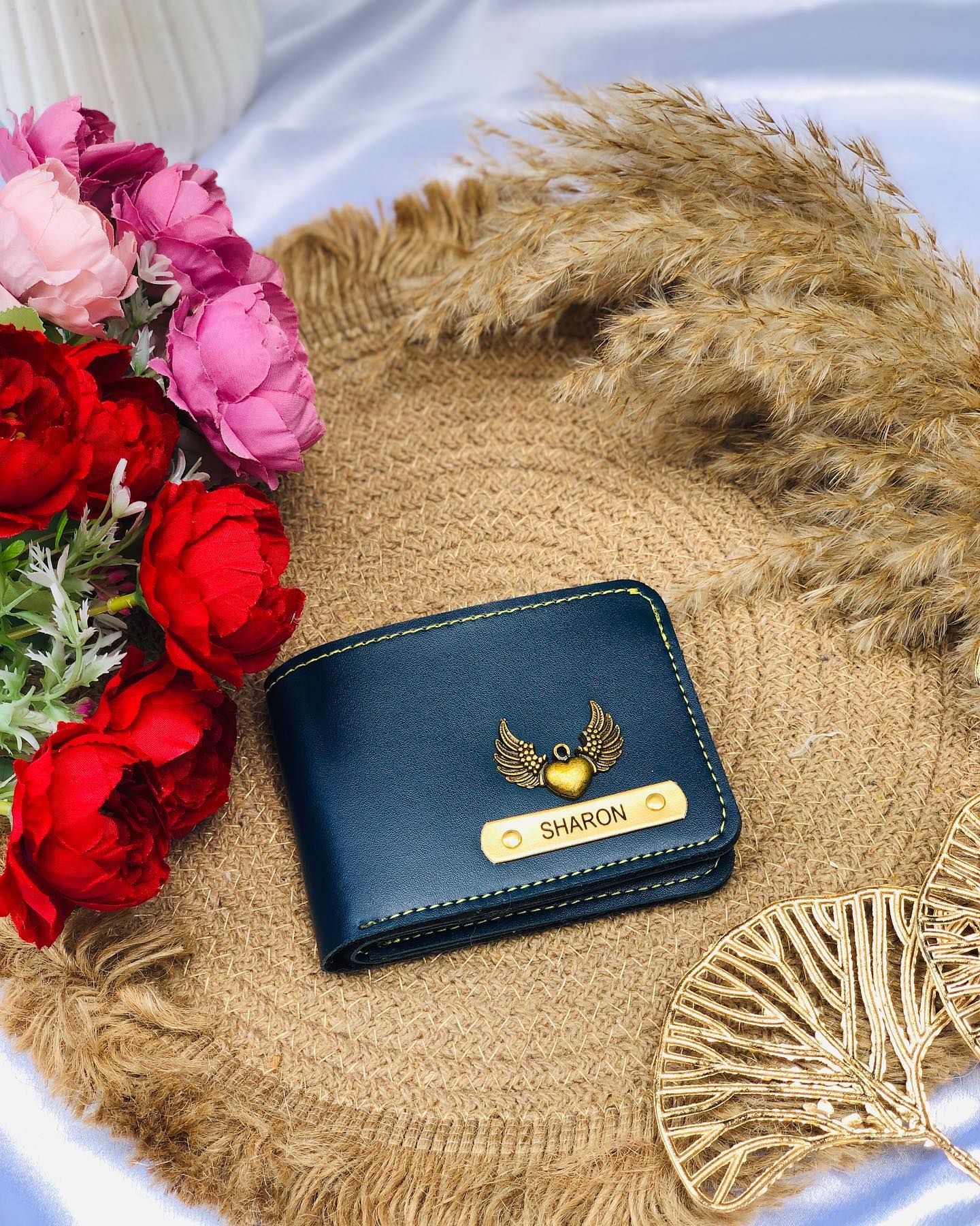 A navy leather wallet engraved with a name and finished with a gold angel-wing heart charm.