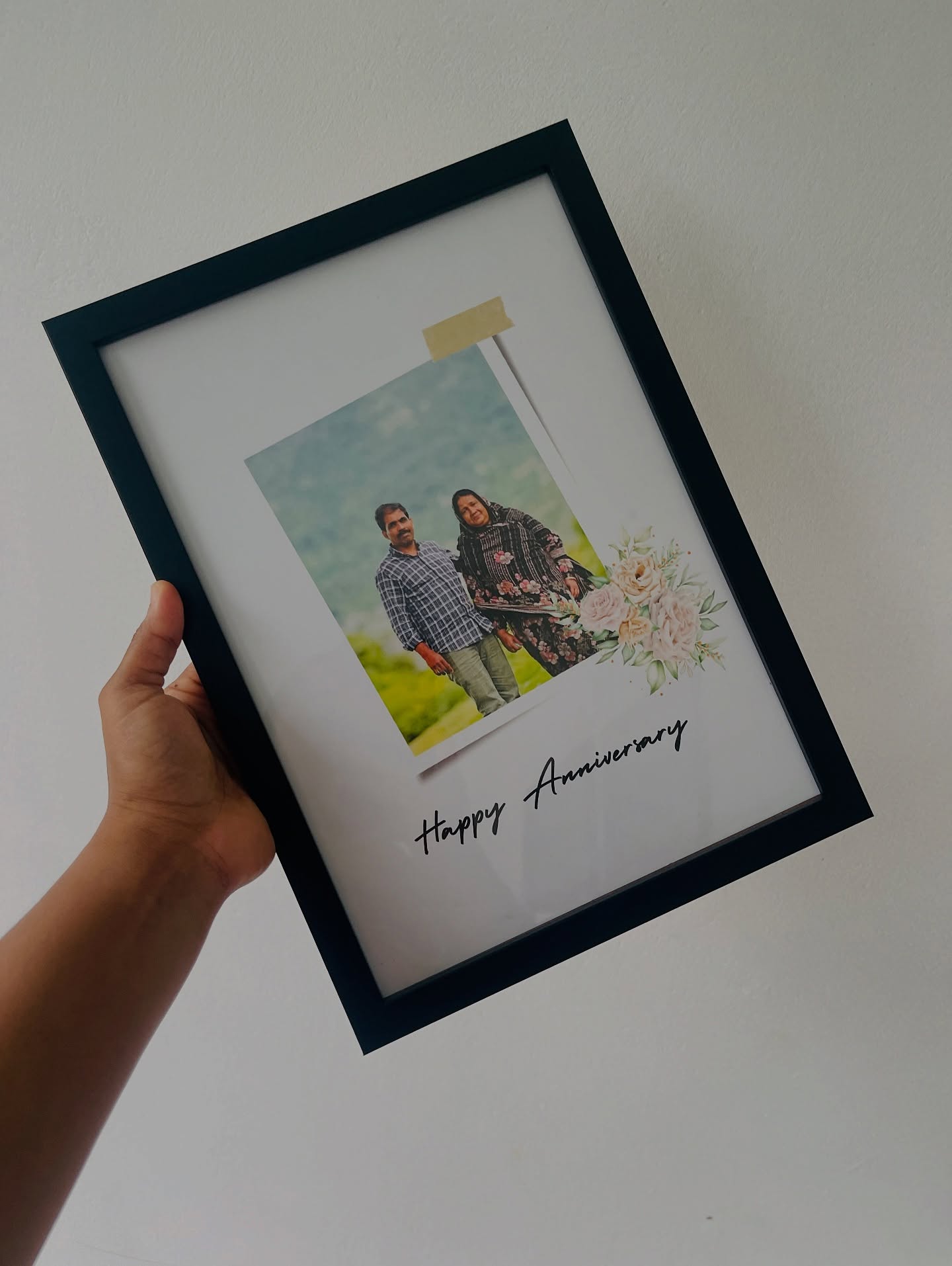 A black photo frame with a printed couple portrait and a floral 'Happy Anniversary' greeting.