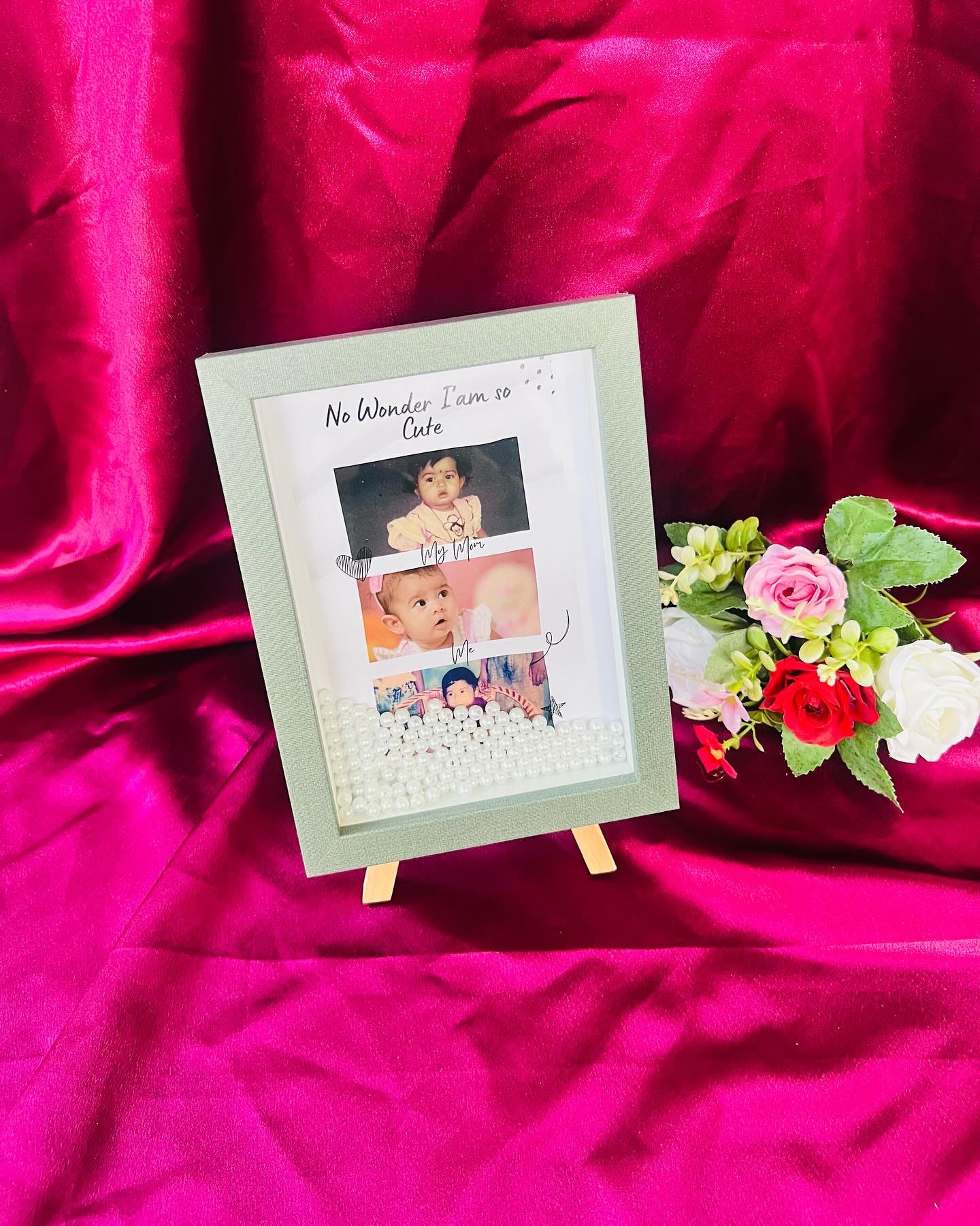 A sage green shadow-box photo frame layered with childhood photos and pearls, captioned "No wonder I am so cute".