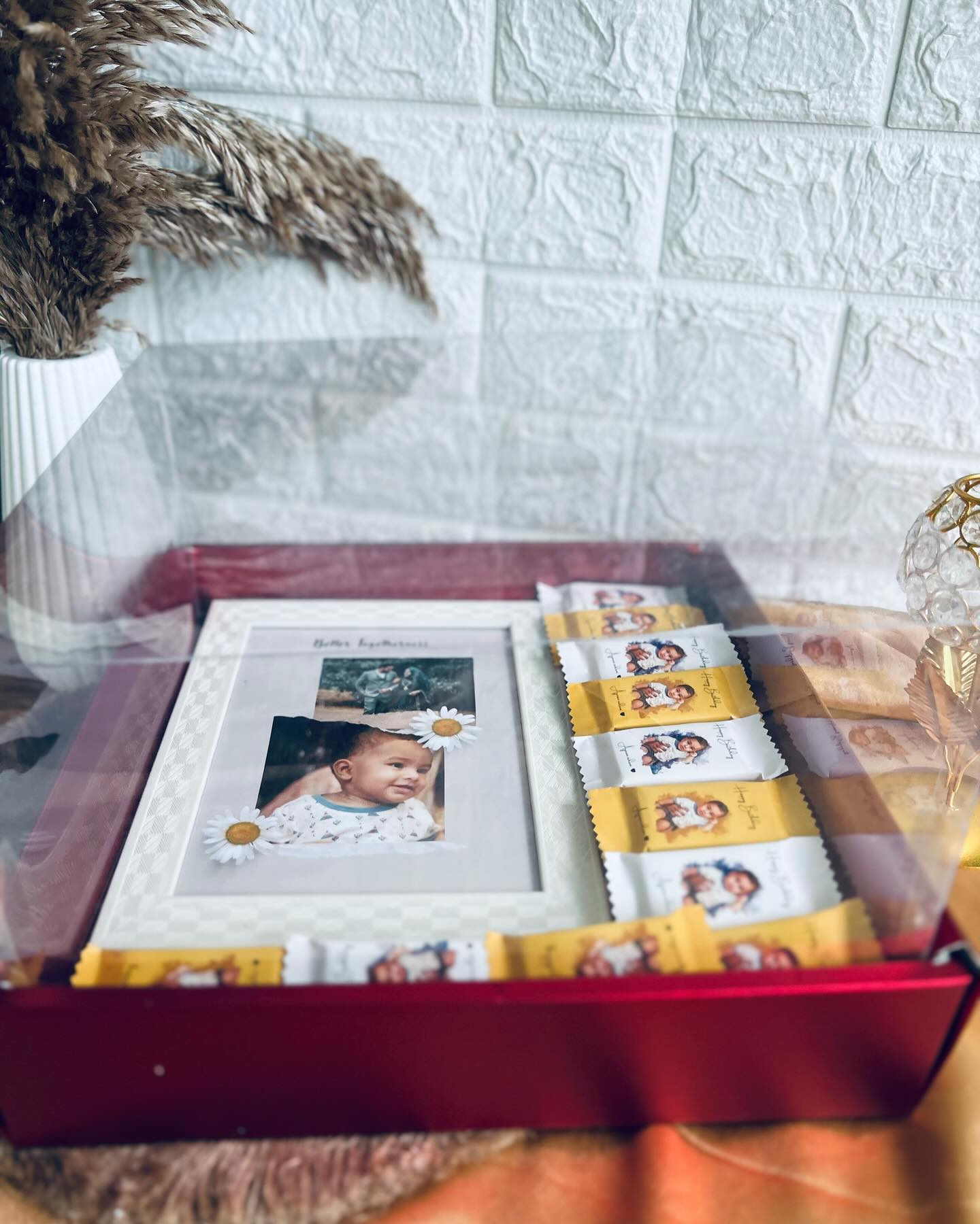 A red keepsake box pairing a sweet family photo frame with a row of personalized 'Happy Birthday' wrapped chocolates.