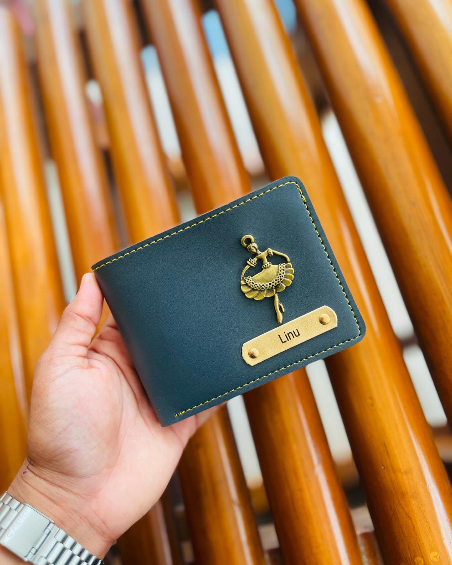 A teal leather wallet with a gold ballerina charm and a personalized name tag.