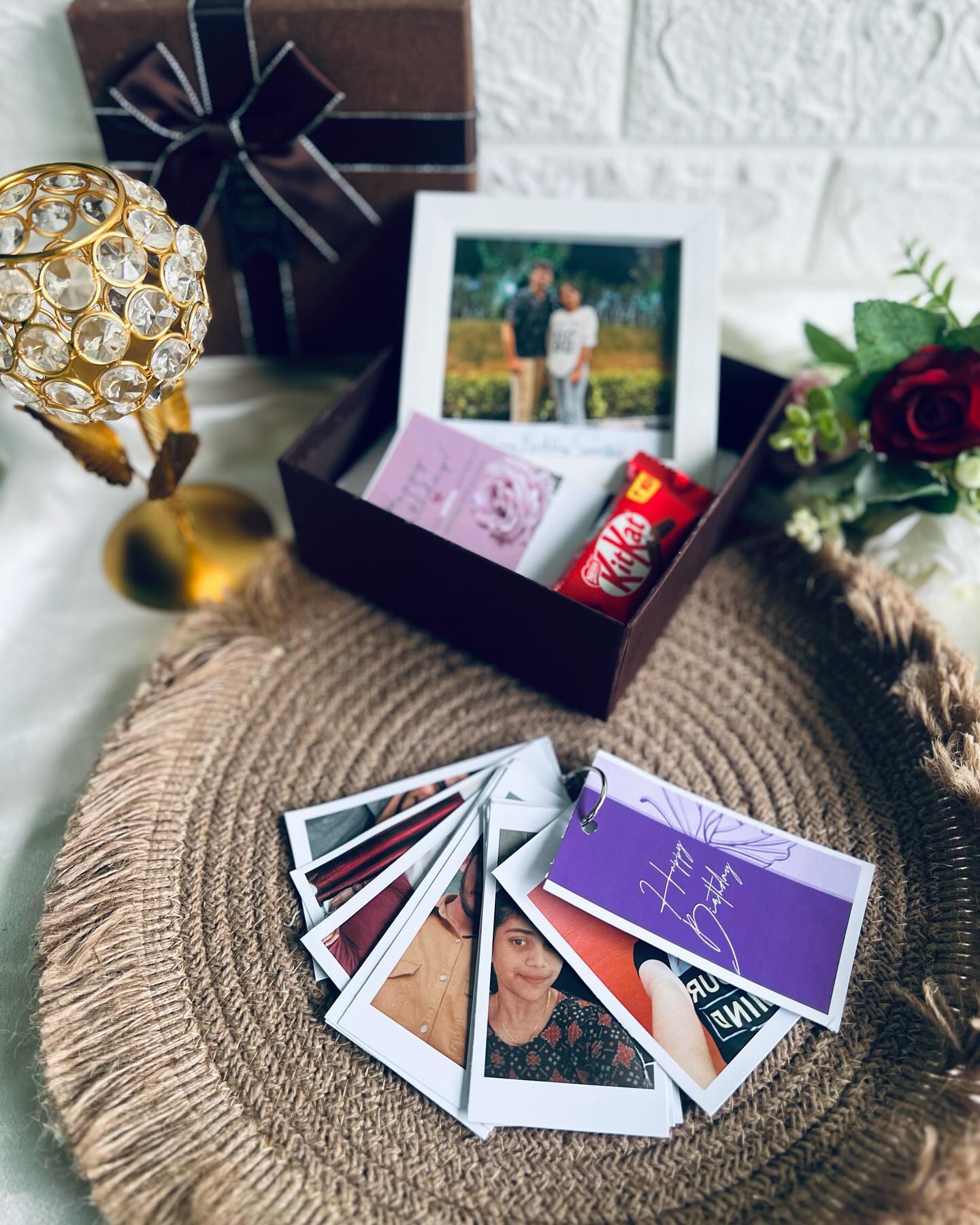 A curated birthday gift set with a ribbon-tied box, a personalized photo frame, and a fan of polaroid keepsakes.