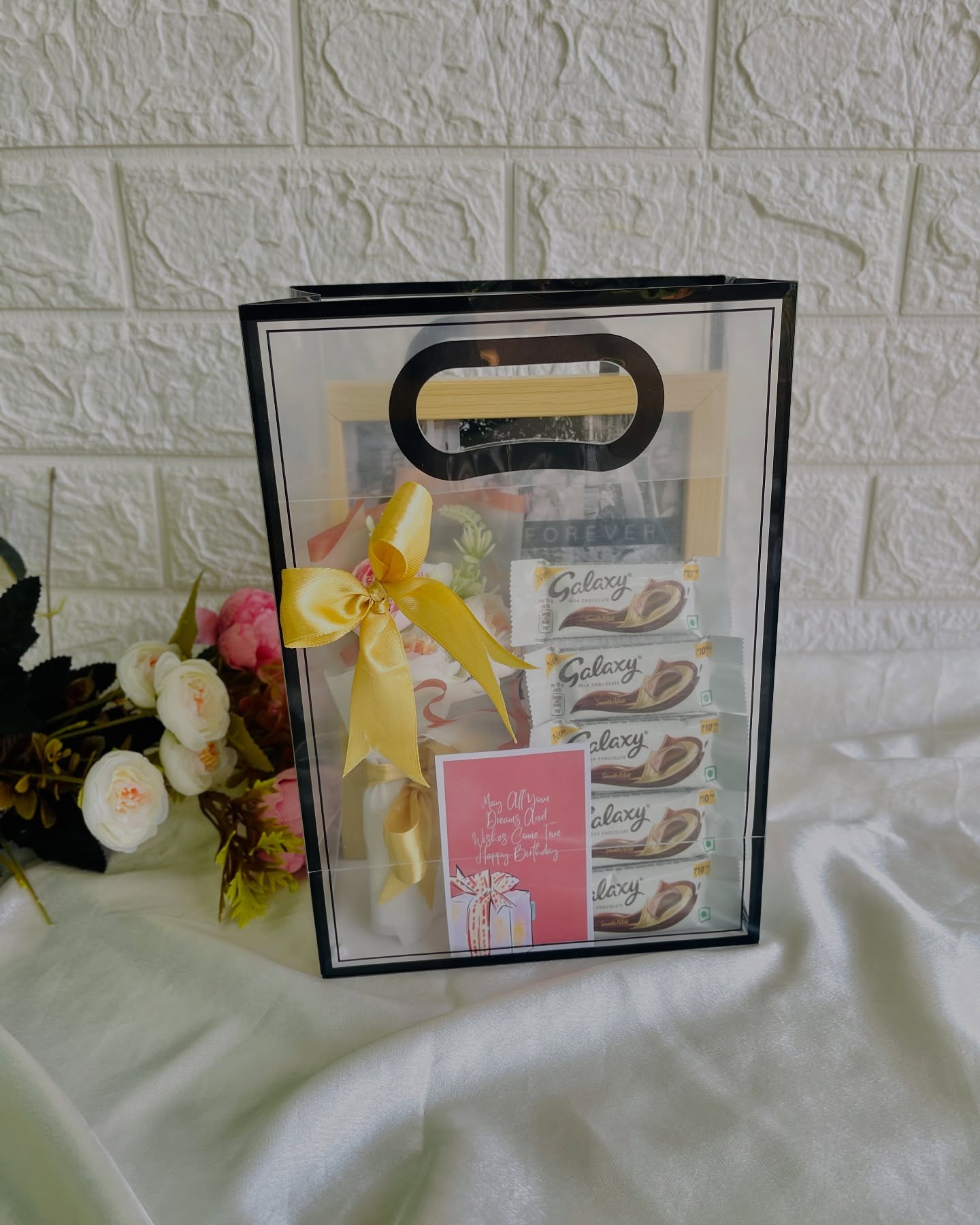 A clear gift bag with a personalized photo frame, Galaxy chocolate bars, and a birthday wish card.