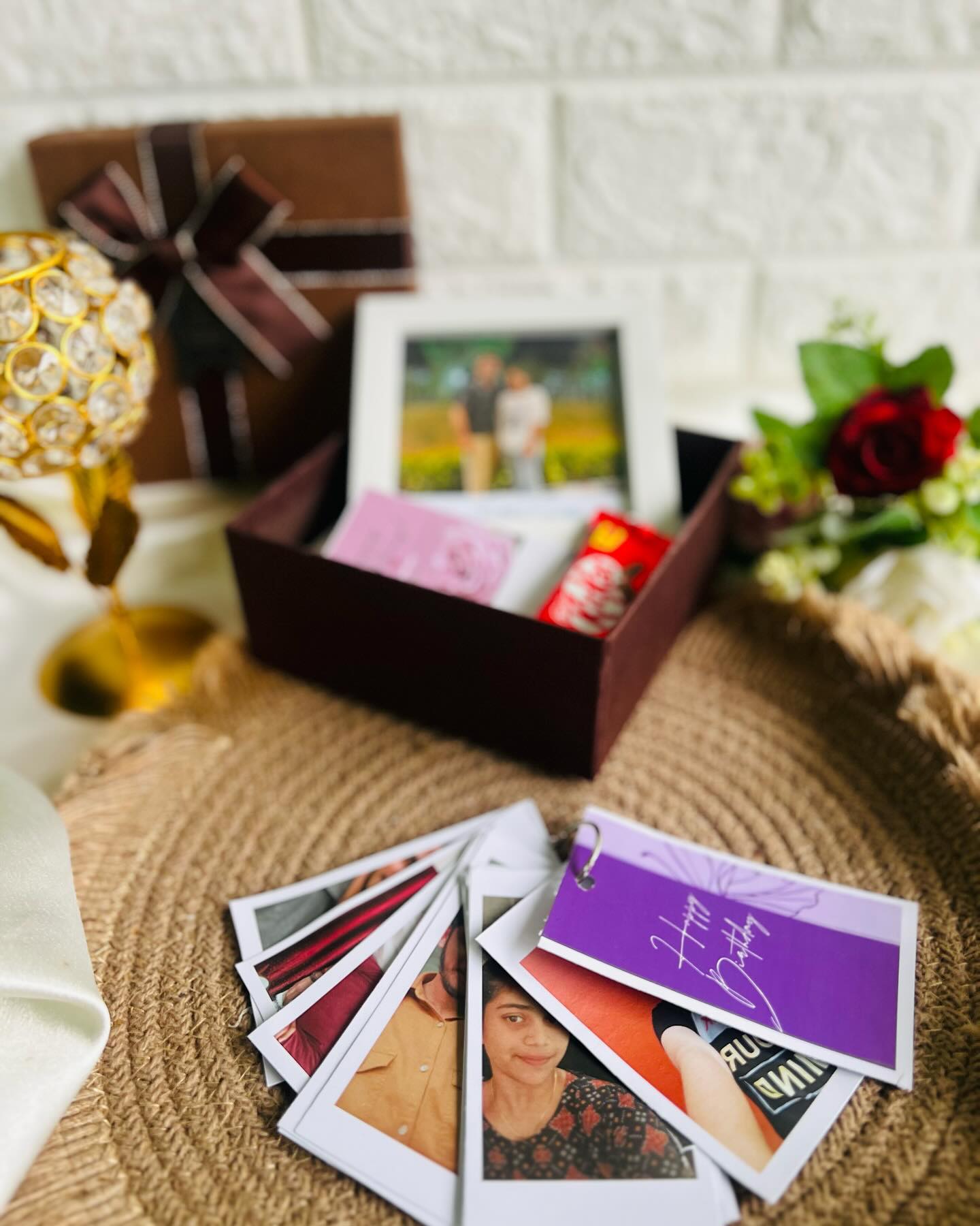A gift box paired with a fan of polaroid-style photo cards and a personalized 'Happy Birthday' photo book tag.