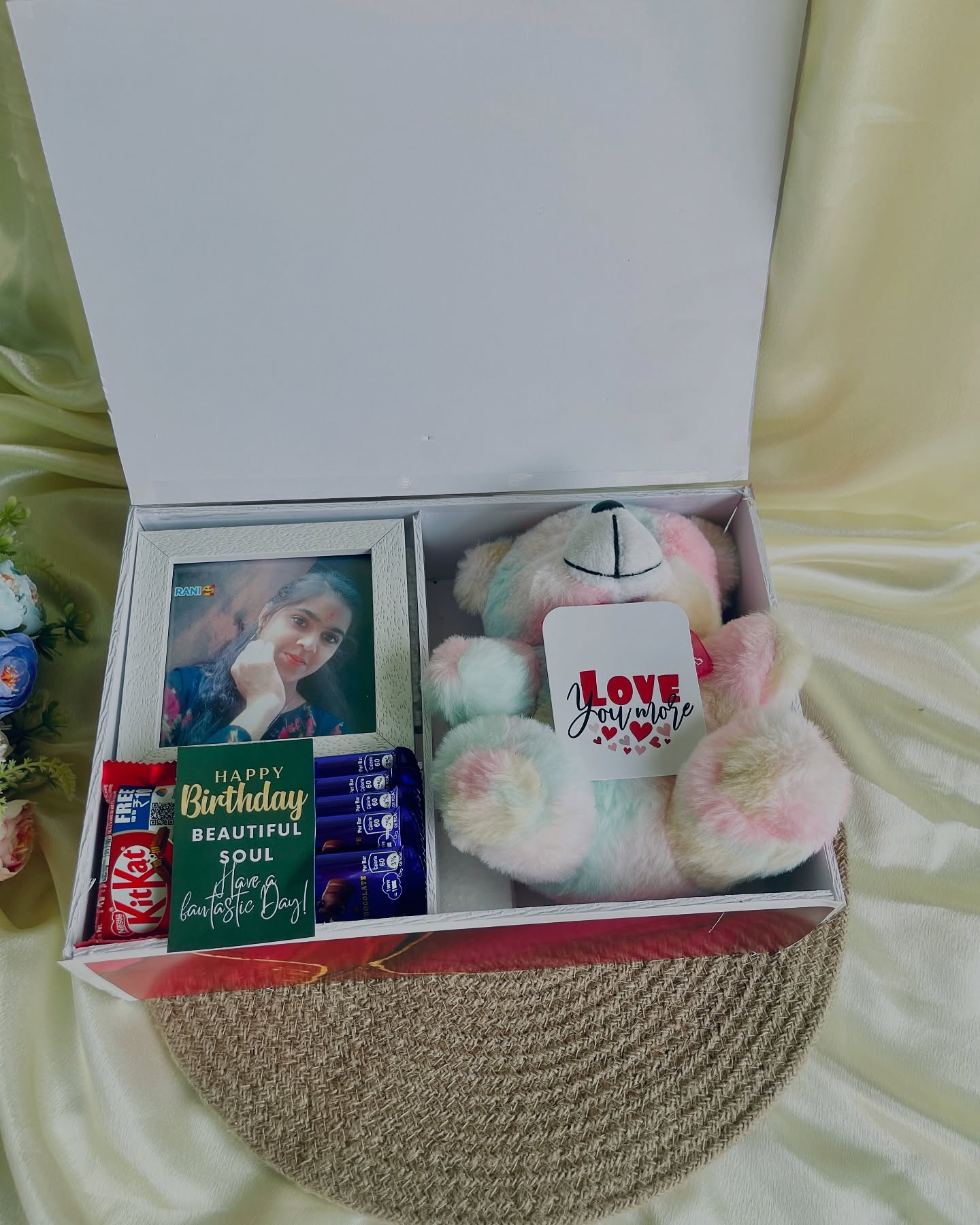 A gift box with a pastel teddy bear, personalized photo frame, and assorted chocolates for a birthday surprise.