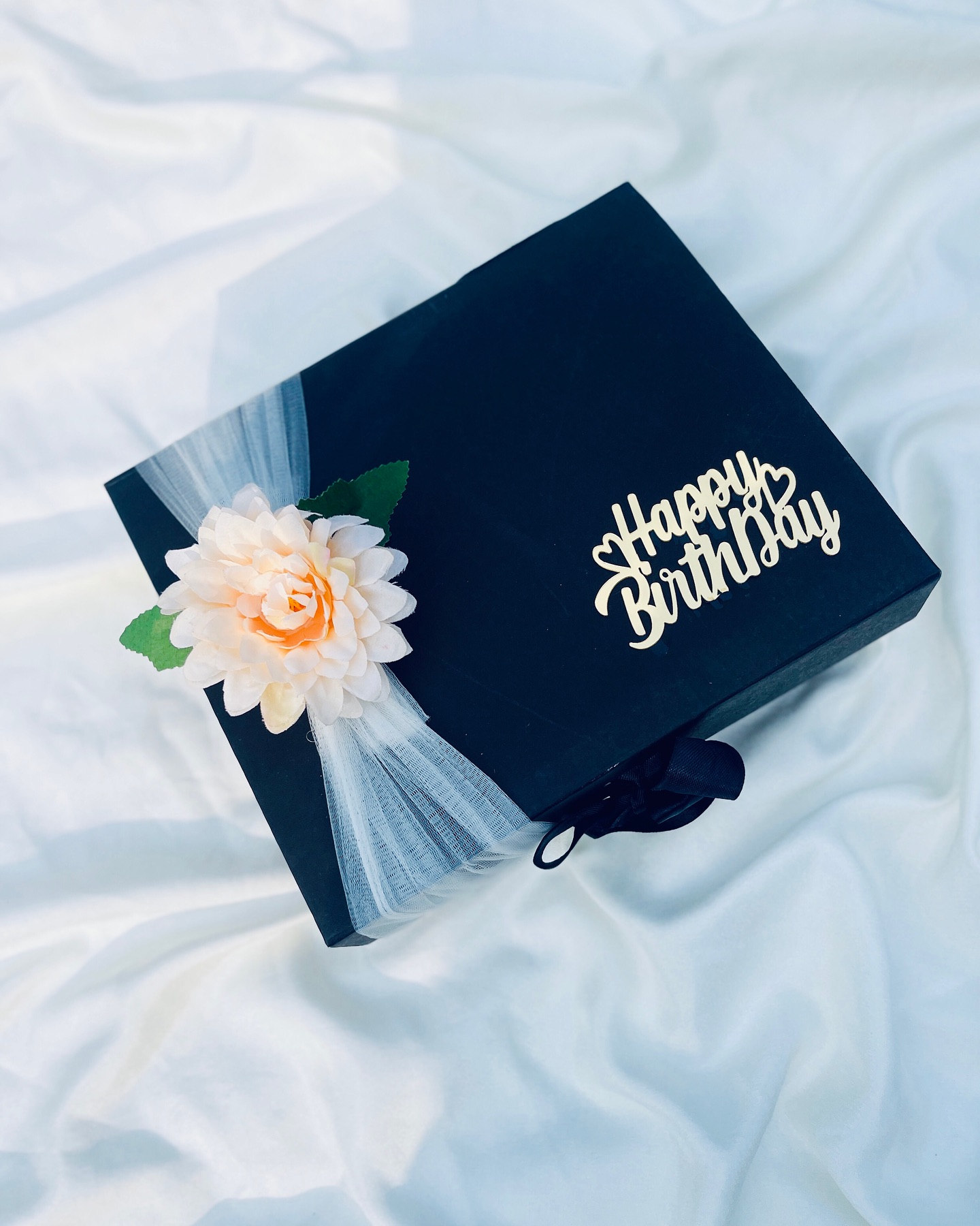 An elegant black gift box finished with a blush flower and tulle bow, topped with a 'Happy Birthday' cut-out.