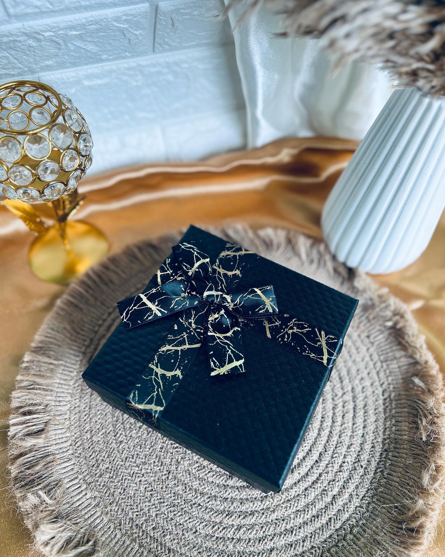 A sleek black textured gift box finished with a black-and-gold marble-print ribbon bow.