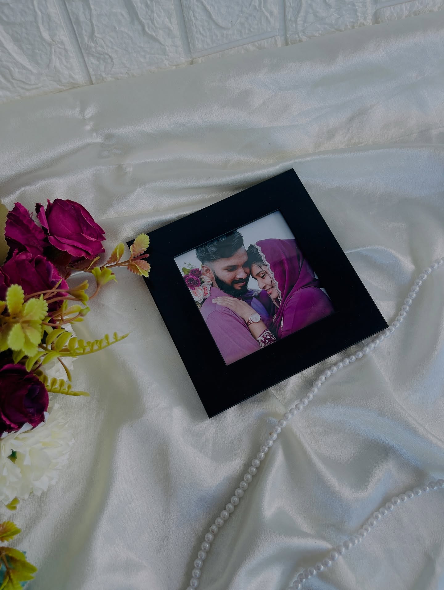 A compact black-framed custom couple photo styled with burgundy florals and a pearl strand.