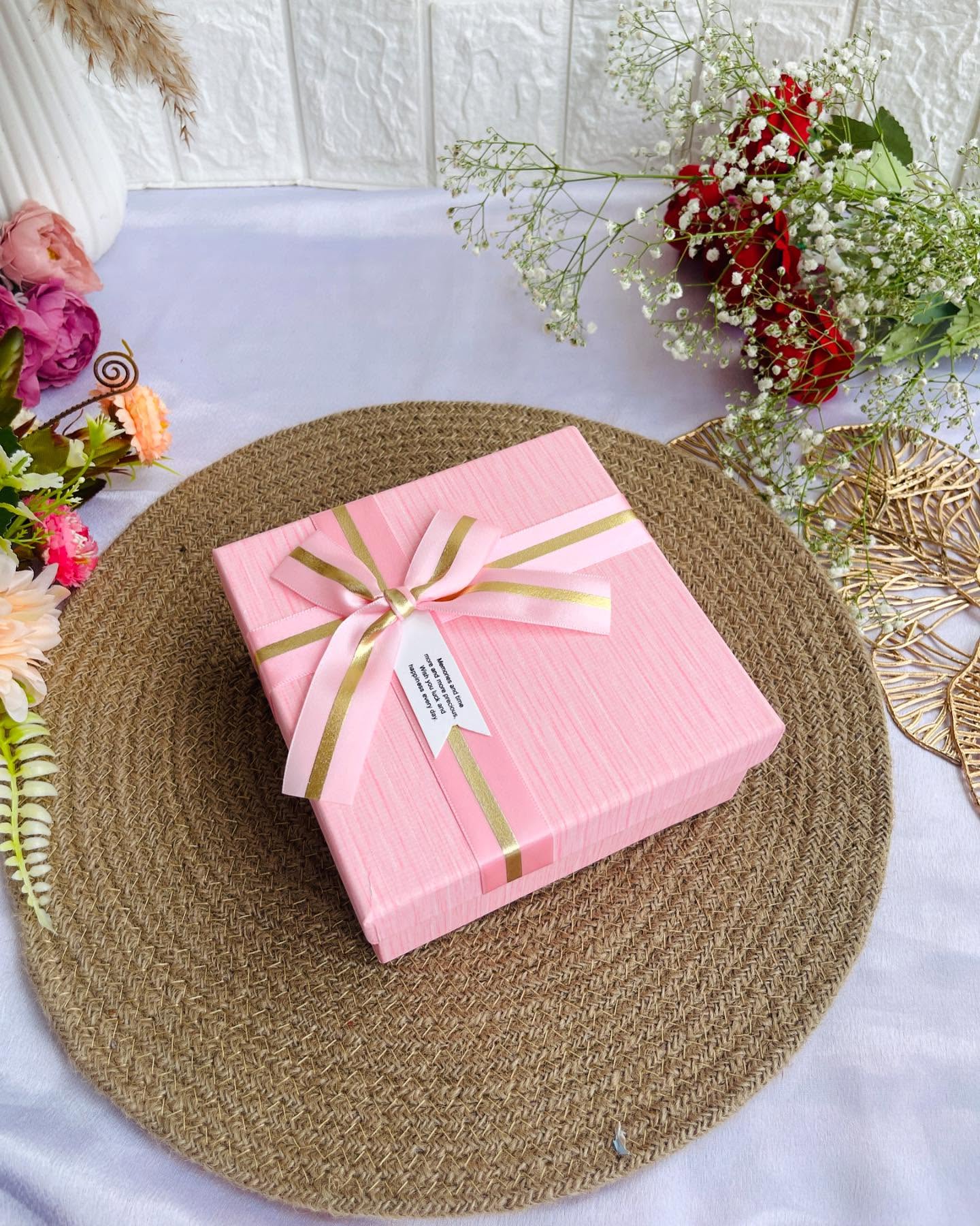 An elegantly wrapped blush pink gift box finished with a satin and gold ribbon bow and a heartfelt message tag.