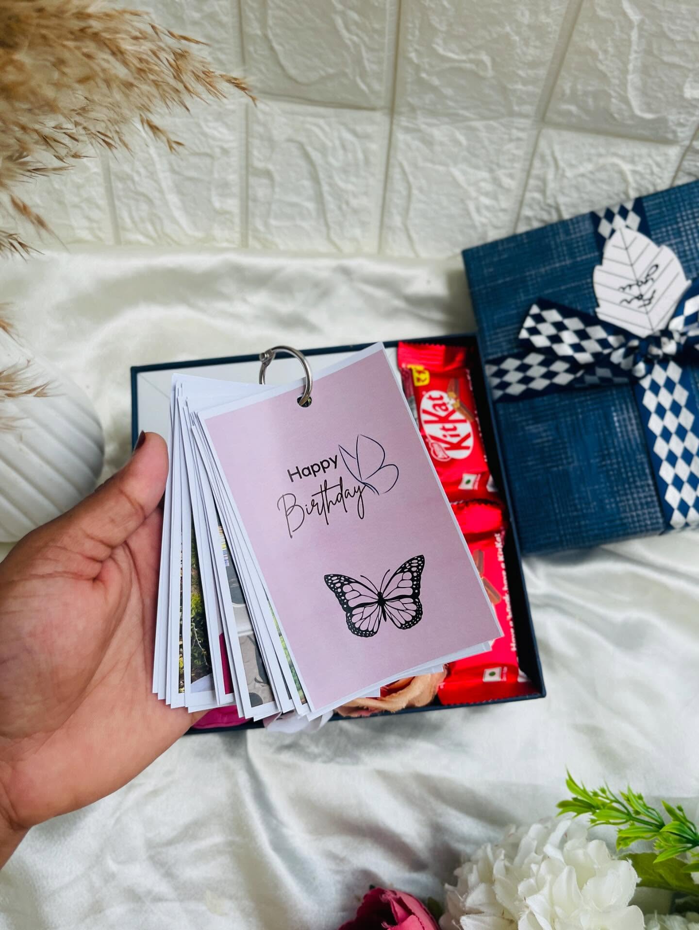 A ring-bound butterfly-themed photo album paired with KitKat chocolates in a navy checkered birthday gift box.