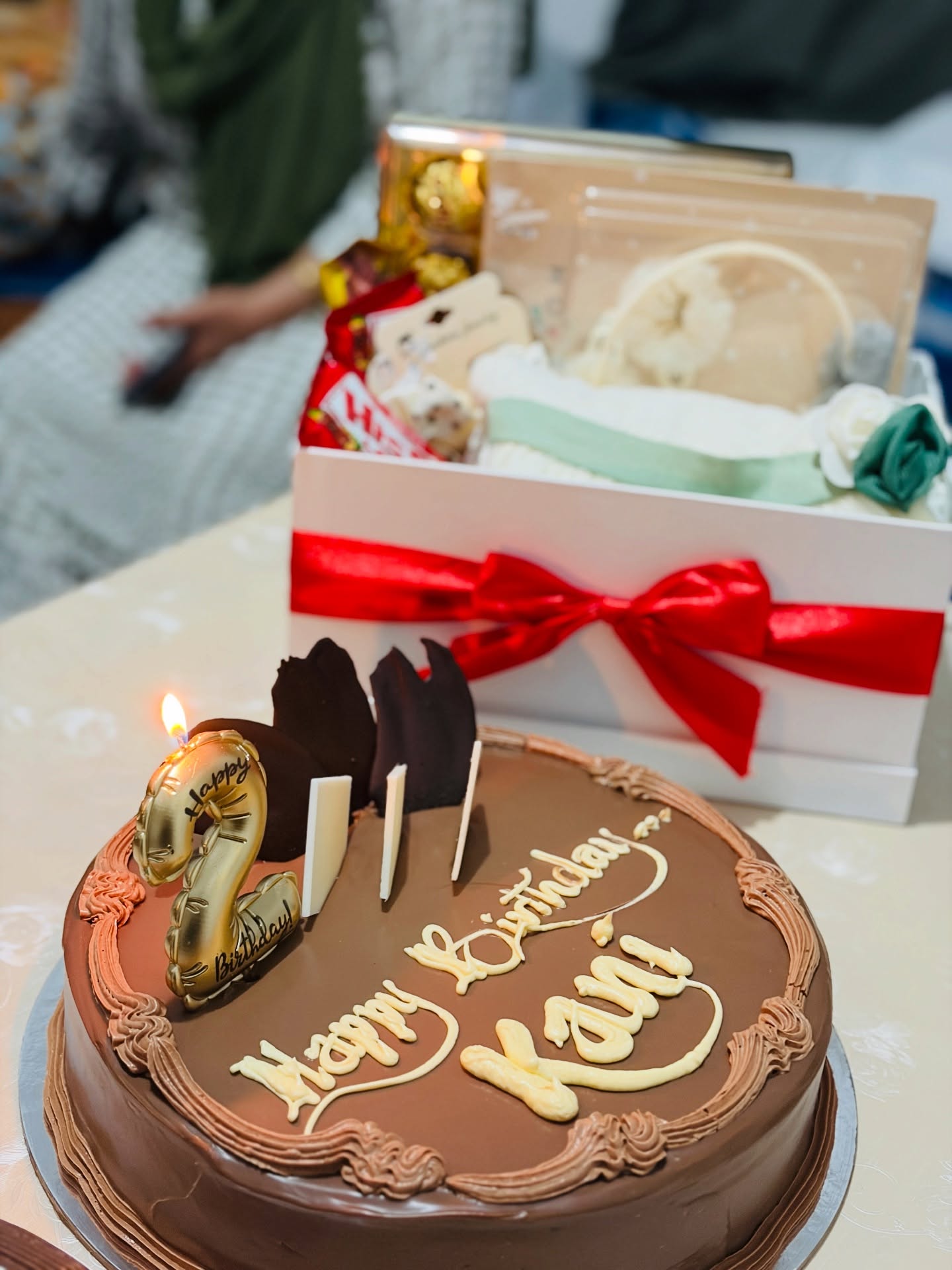 A ribboned gift box filled with assorted chocolates and treats, paired with a birthday cake for a full celebration set.