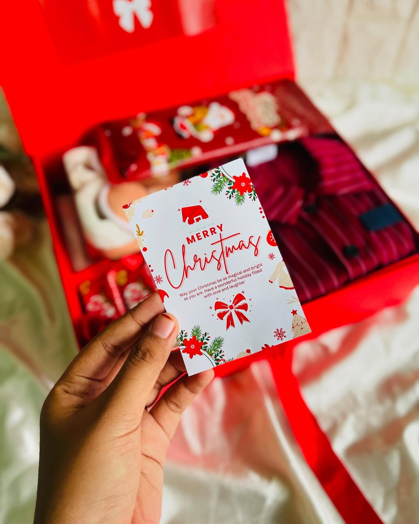 A festive red gift box layered with cosy pajamas, holiday treats and a Merry Christmas card.