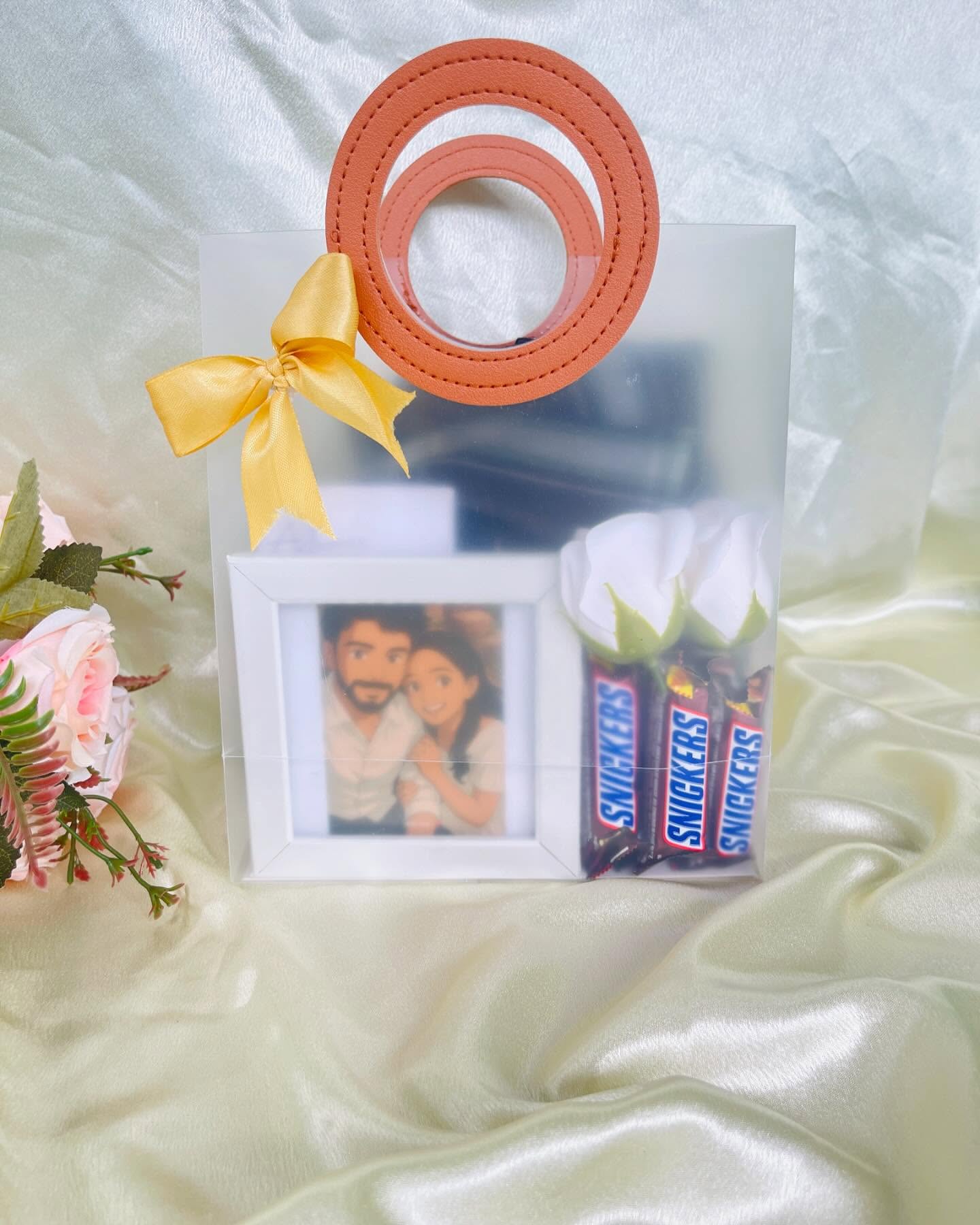 A clear gift bag with a leather-look handle, a mini couple photo frame and a bundle of Snickers bars.
