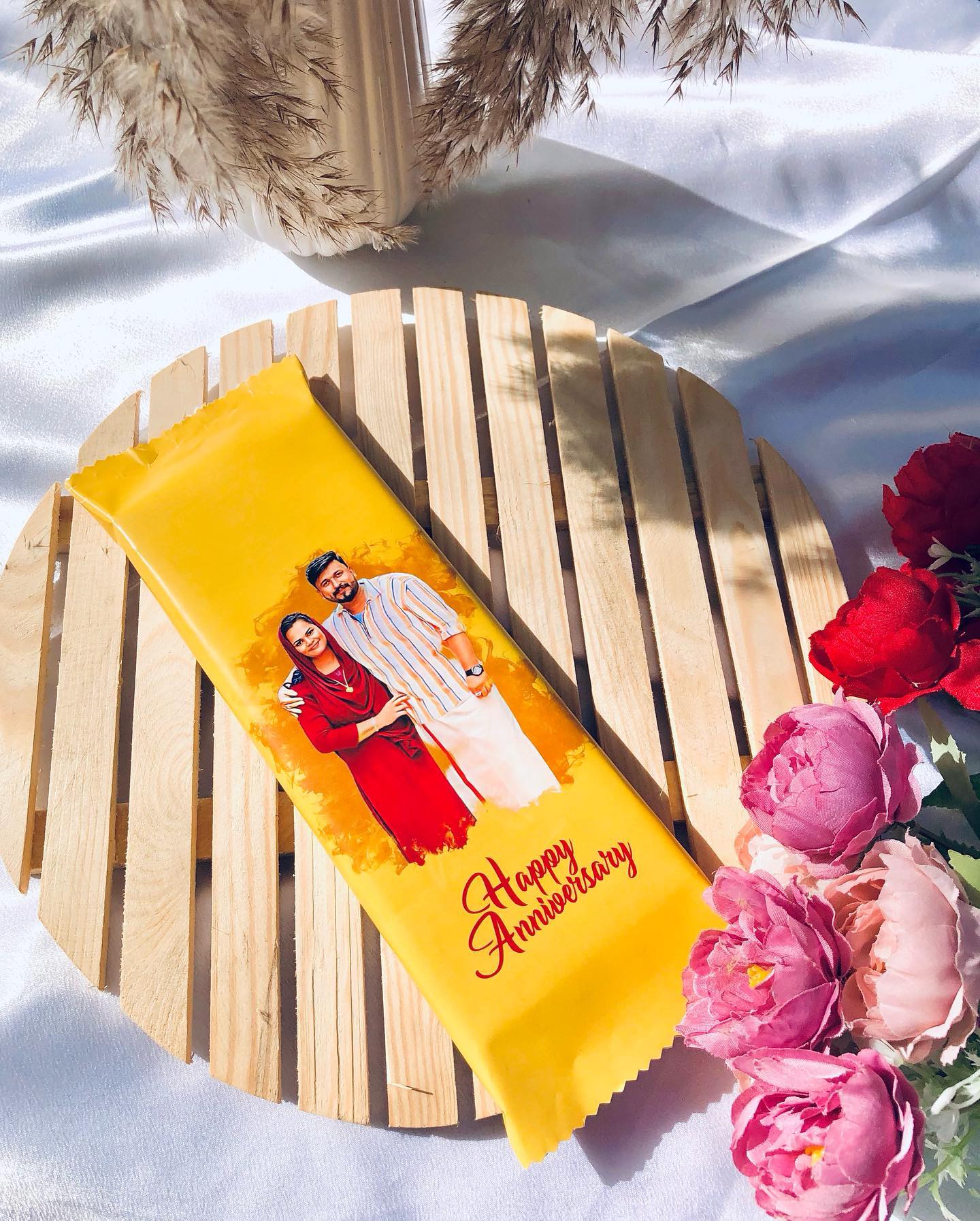 A personalized chocolate bar wrapped with a couple's photo and a sweet 'Happy Anniversary' message.