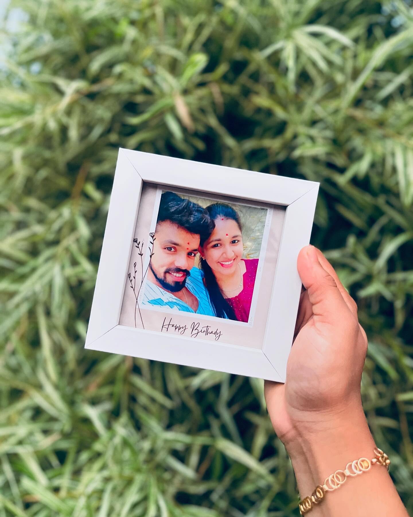 A compact white Polaroid-style frame personalized with a couple's photo and a handwritten 'Happy Birthday' caption.