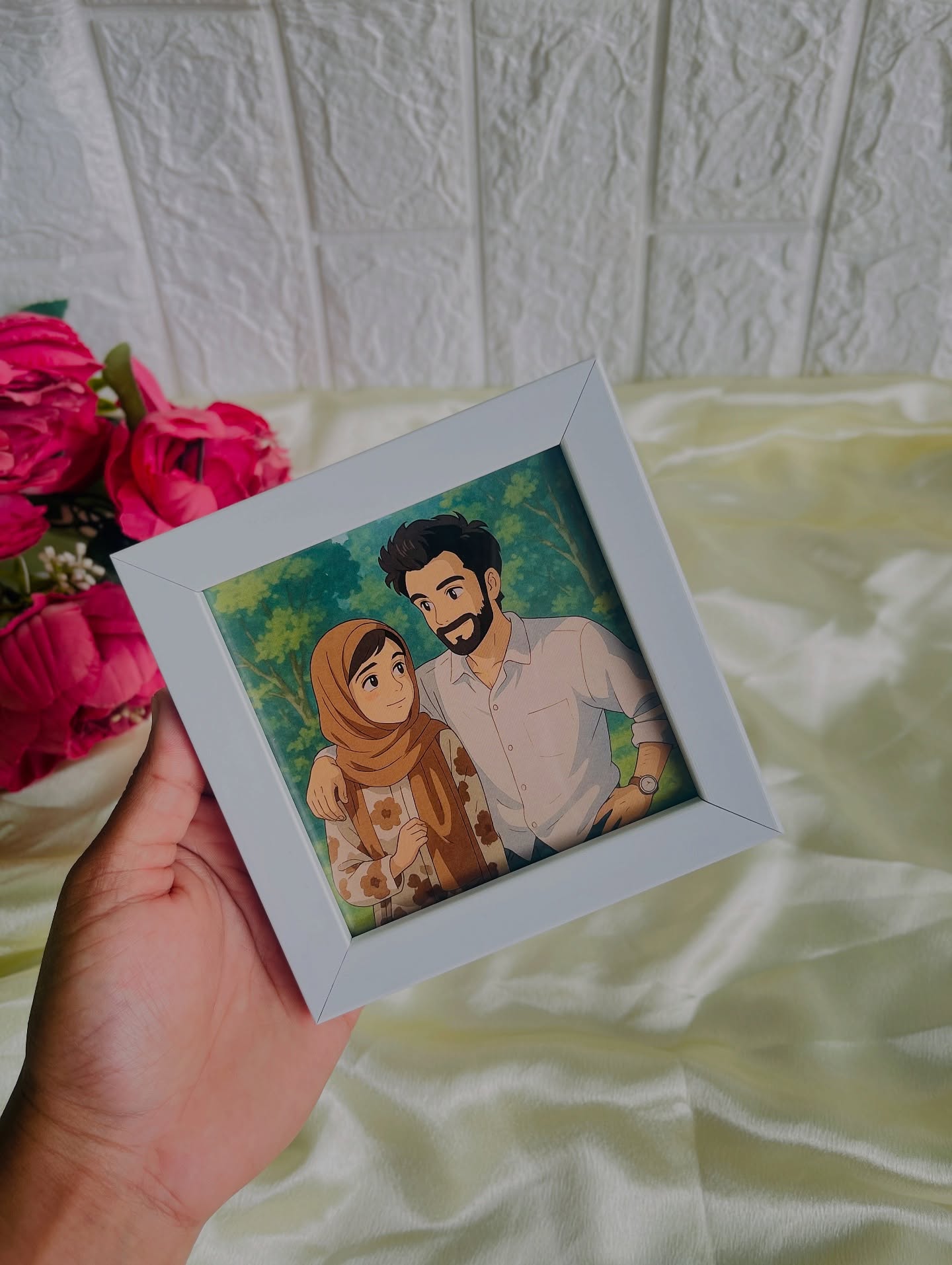 A hand-illustrated custom couple portrait in a sleek white photo frame, paired with a bouquet of pink roses.