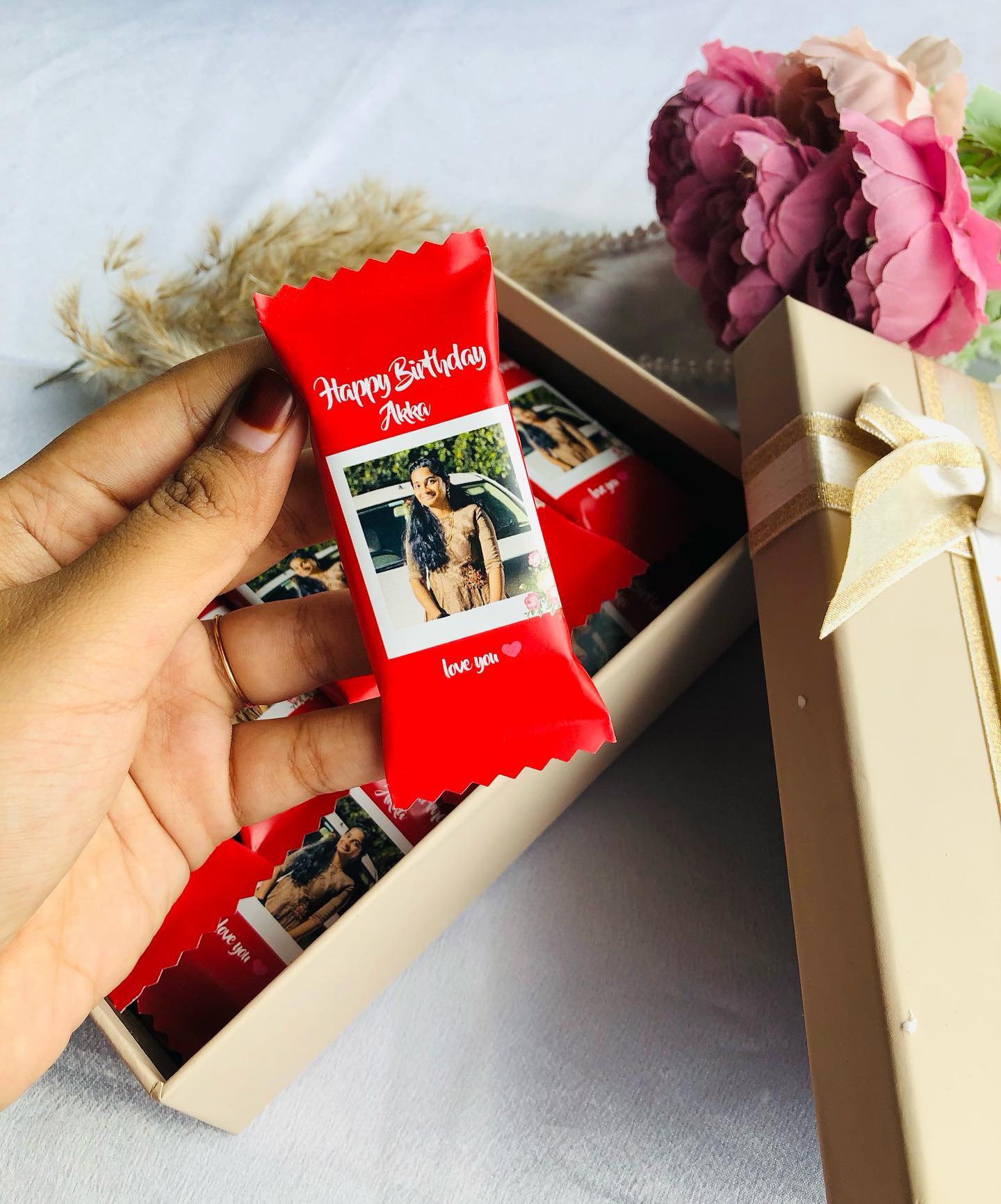 An assortment of personalized chocolate bars printed with a birthday photo and name, boxed with pink peonies.