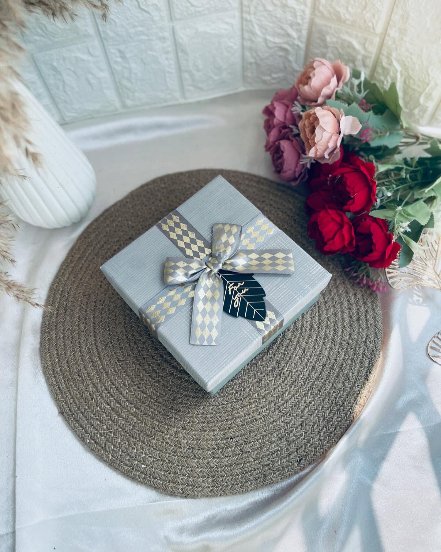 A neatly wrapped grey gift box finished with a diamond-pattern ribbon bow and a 'For You' tag.