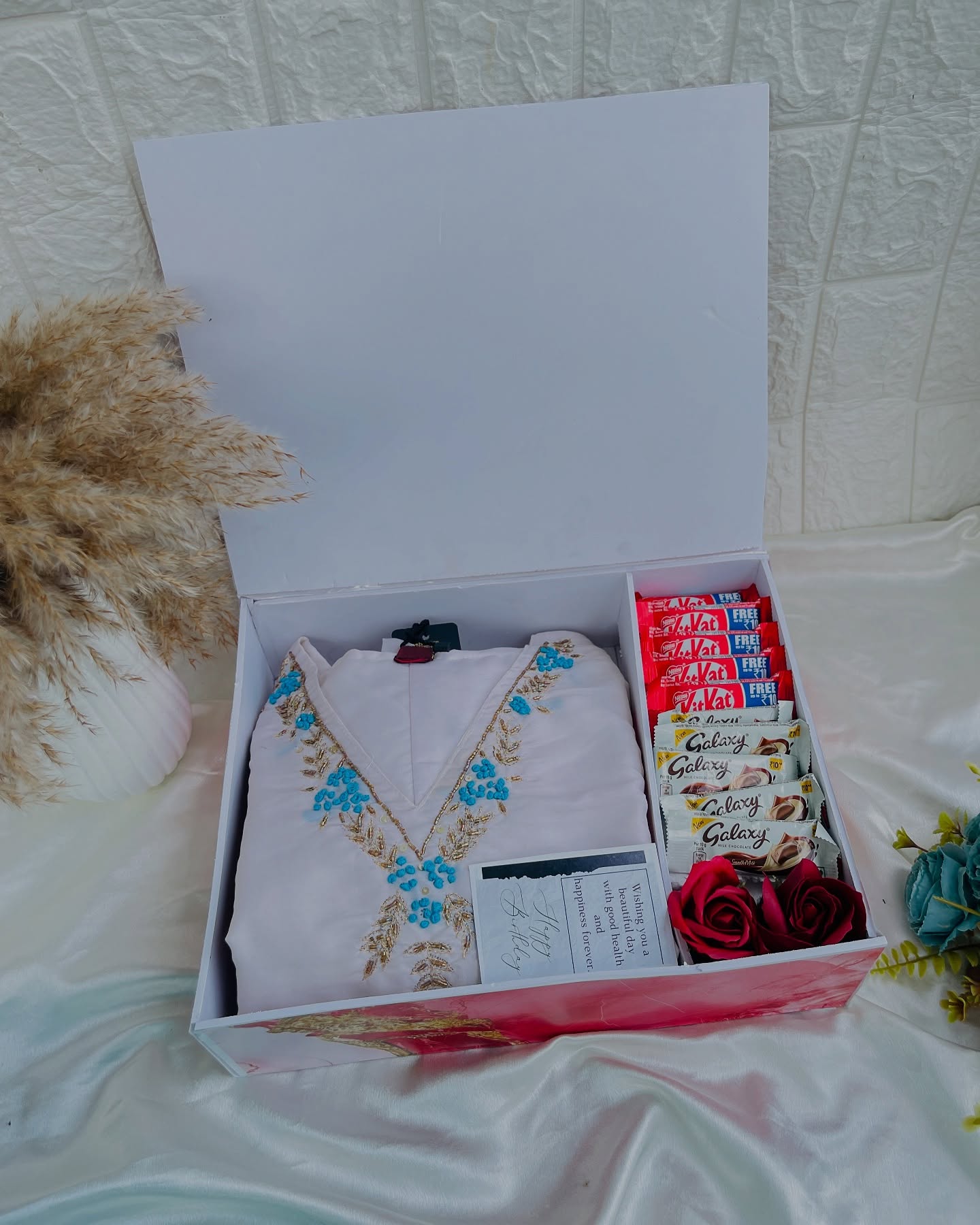 An elegant white gift box pairing a hand-embroidered kurta with KitKat and Galaxy chocolates and fresh roses.