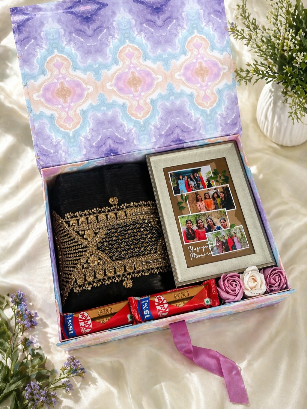 A festive gift box pairing a black gold-embroidered saree with a personalized family photo frame, chocolates, and roses.