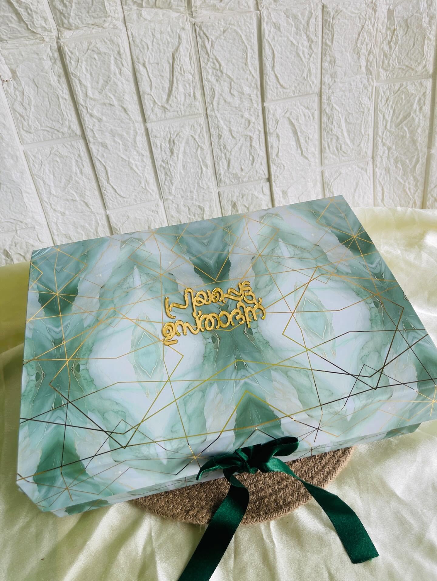 A green marble-effect gift box with gold geometric detailing and a heartfelt wishes message on the lid.