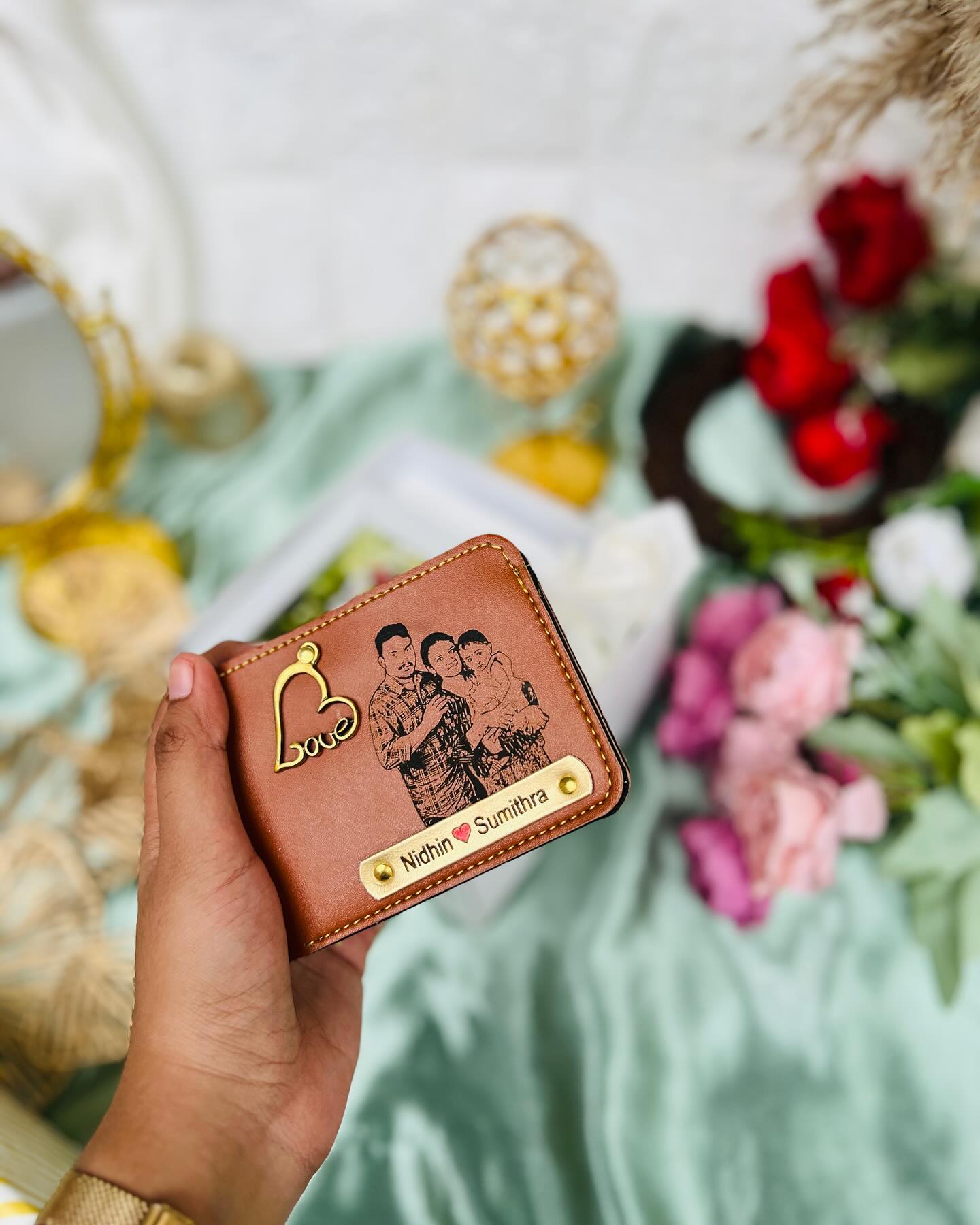 A tan leather wallet engraved with a couple's photo, their names, and a gold heart charm.