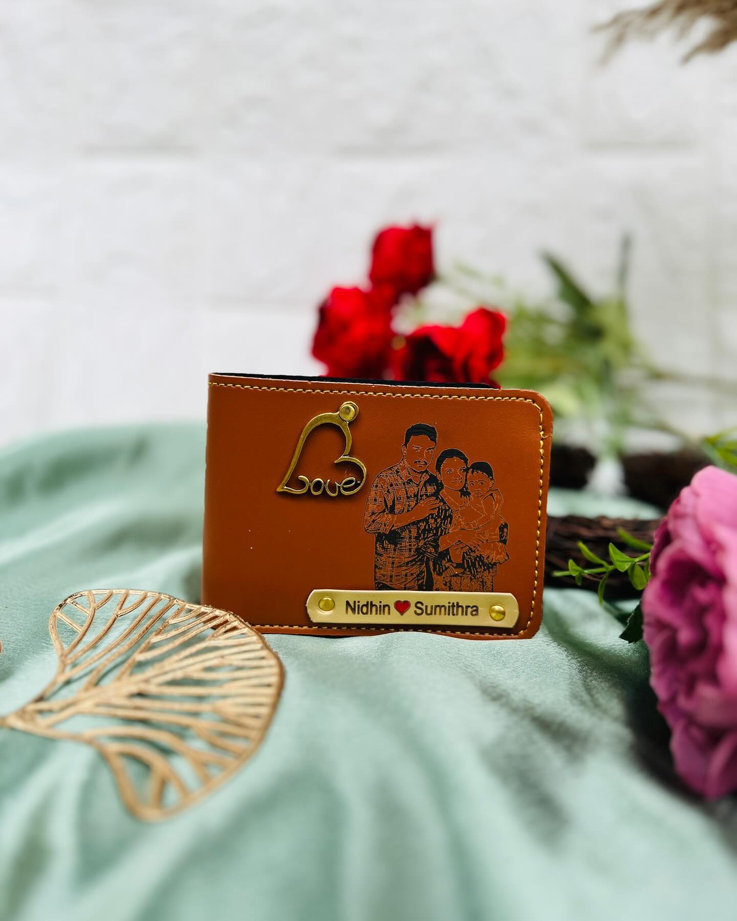 A tan leather wallet custom-engraved with a family portrait and names, finished with a gold Love charm.