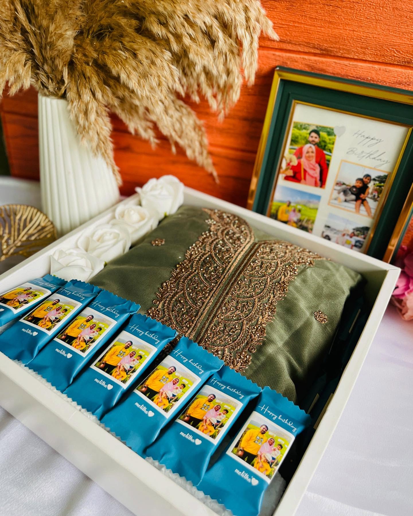 A birthday hamper with a green wooden photo-collage frame and a row of personalized chocolate bars printed with family photos and a name.