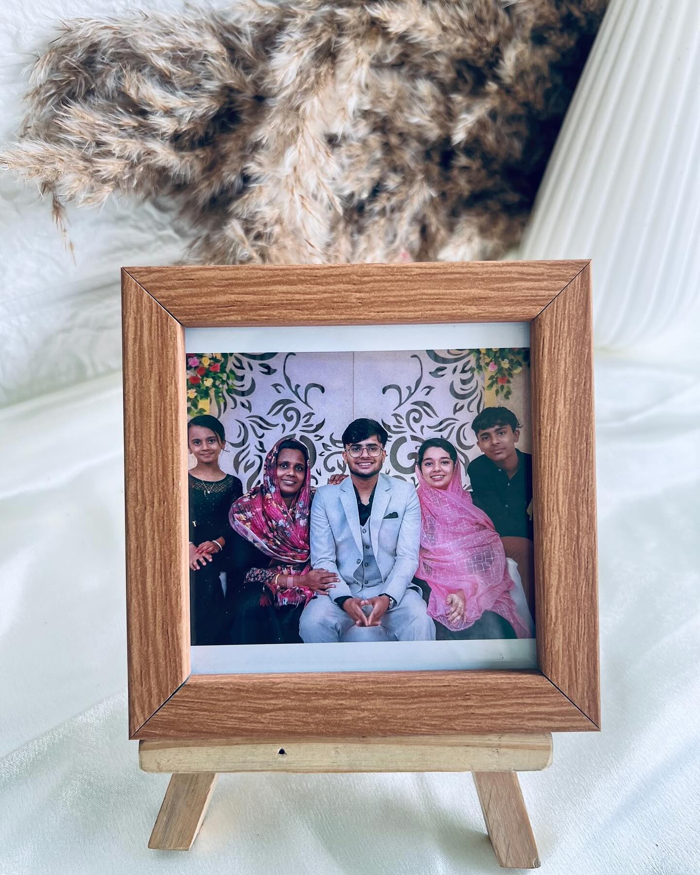 A warm wood-toned photo frame on a mini wooden easel stand, personalized with a family portrait.