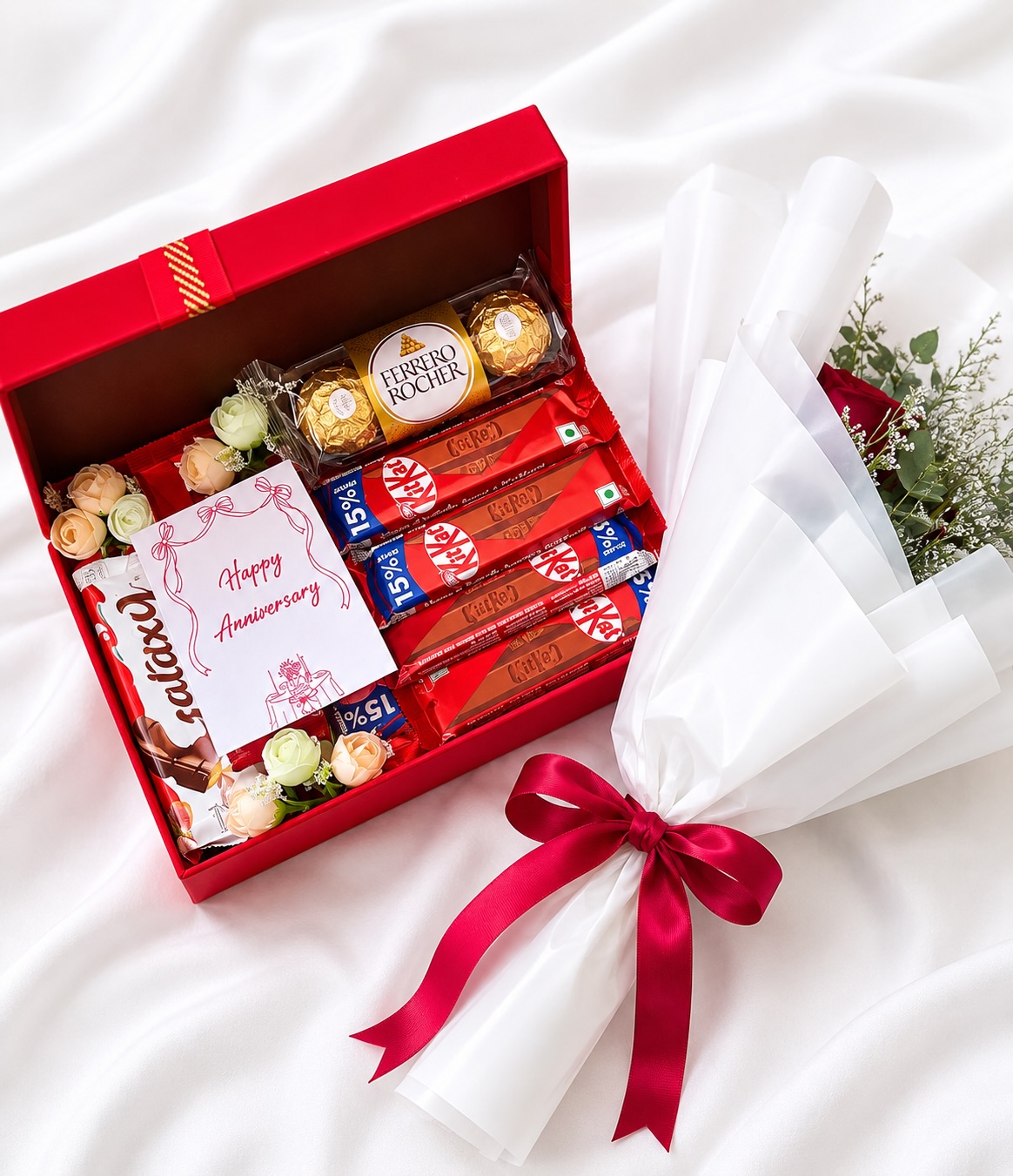 A red gift box filled with Ferrero Rocher, KitKat and Cadbury chocolates alongside a wrapped rose bouquet.