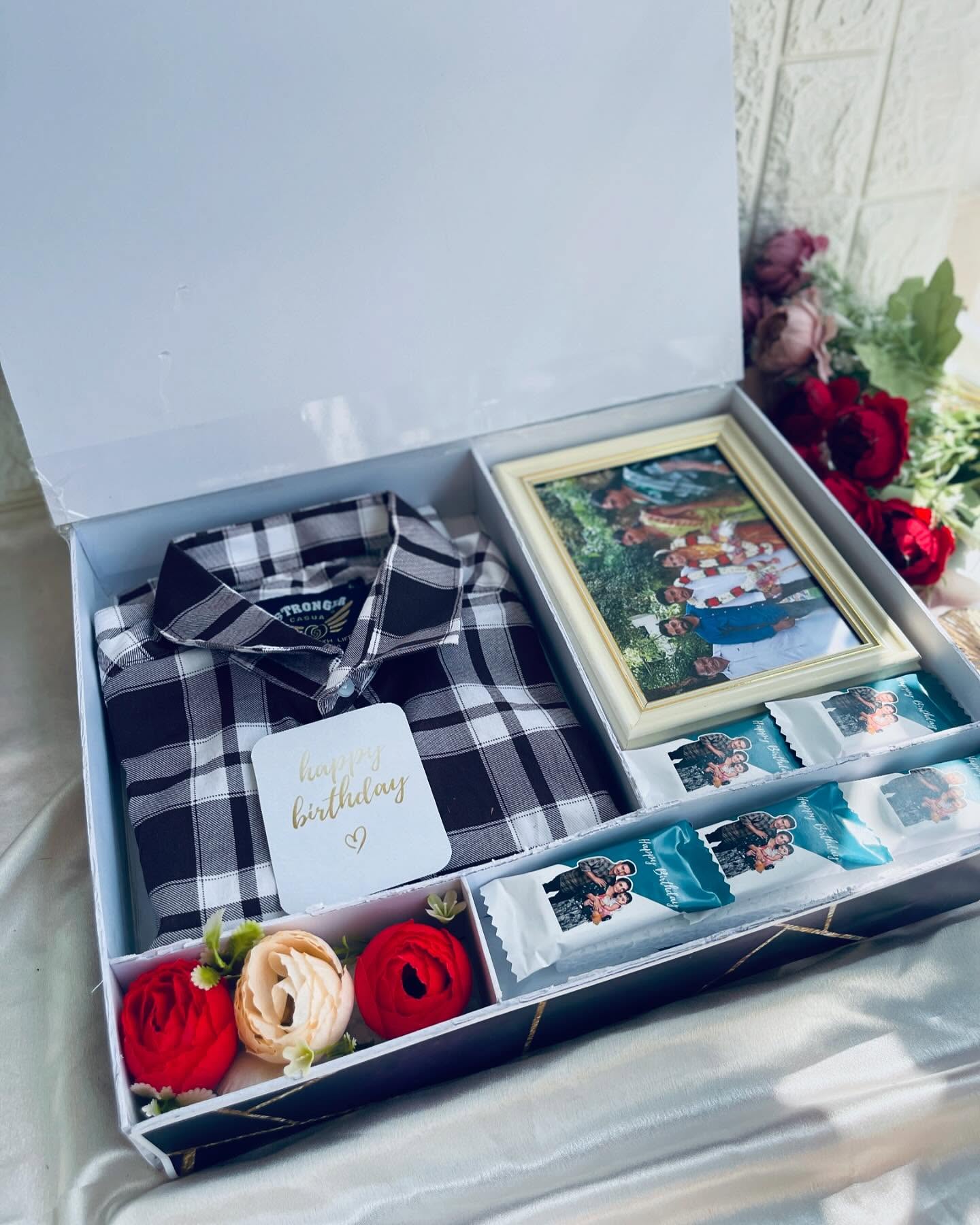 A birthday gift box with a checked flannel shirt, a framed family photo and personalized photo chocolates.