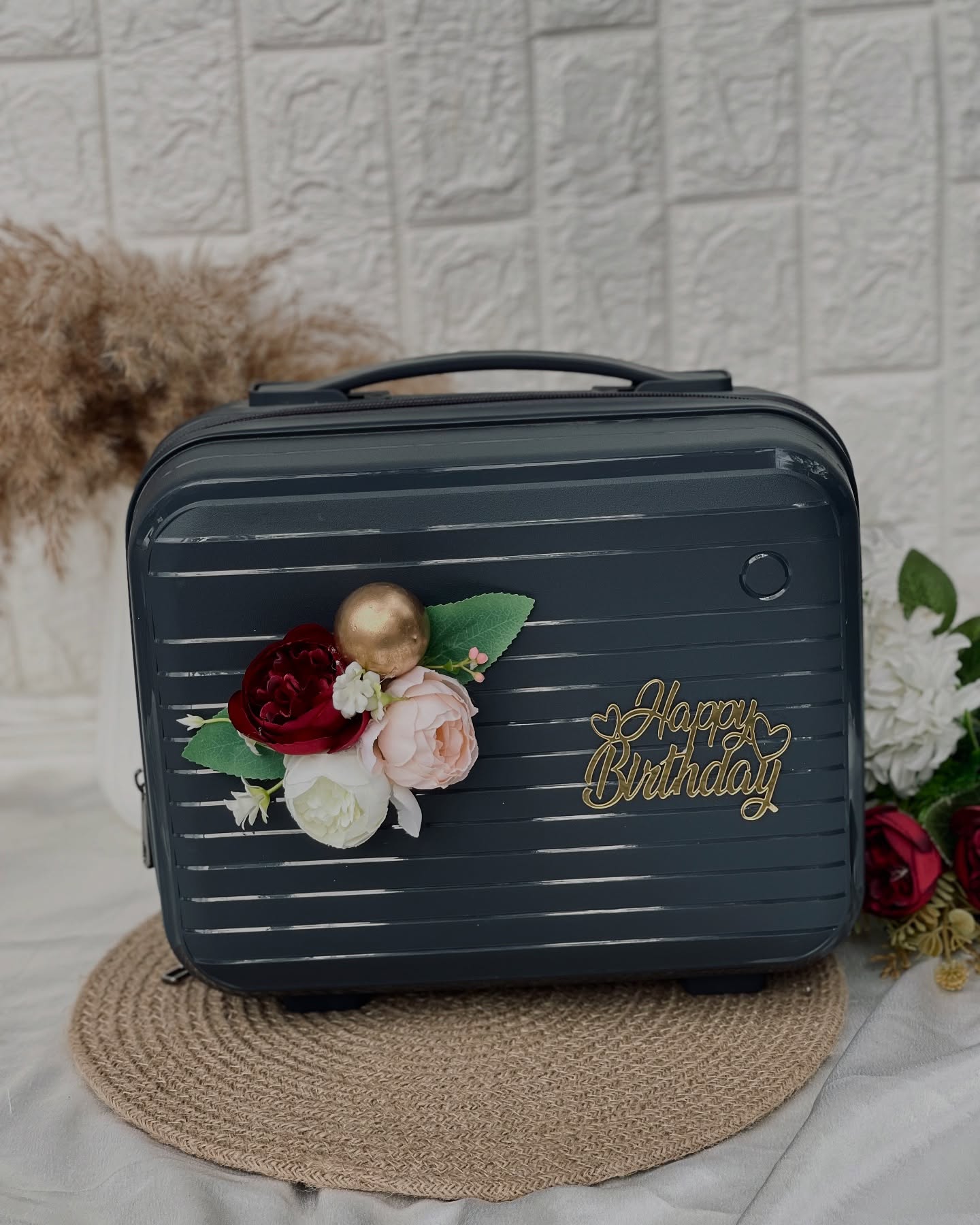 A sleek grey vanity case adorned with a burgundy and blush floral cluster and a gold Happy Birthday charm.