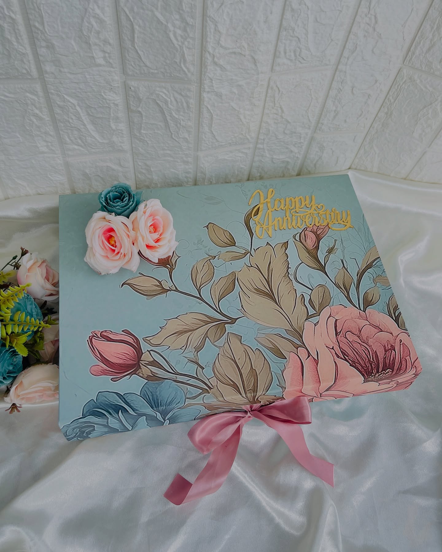 A soft teal gift box hand-painted with roses and a gold 'Happy Anniversary' topper, finished with a satin ribbon.