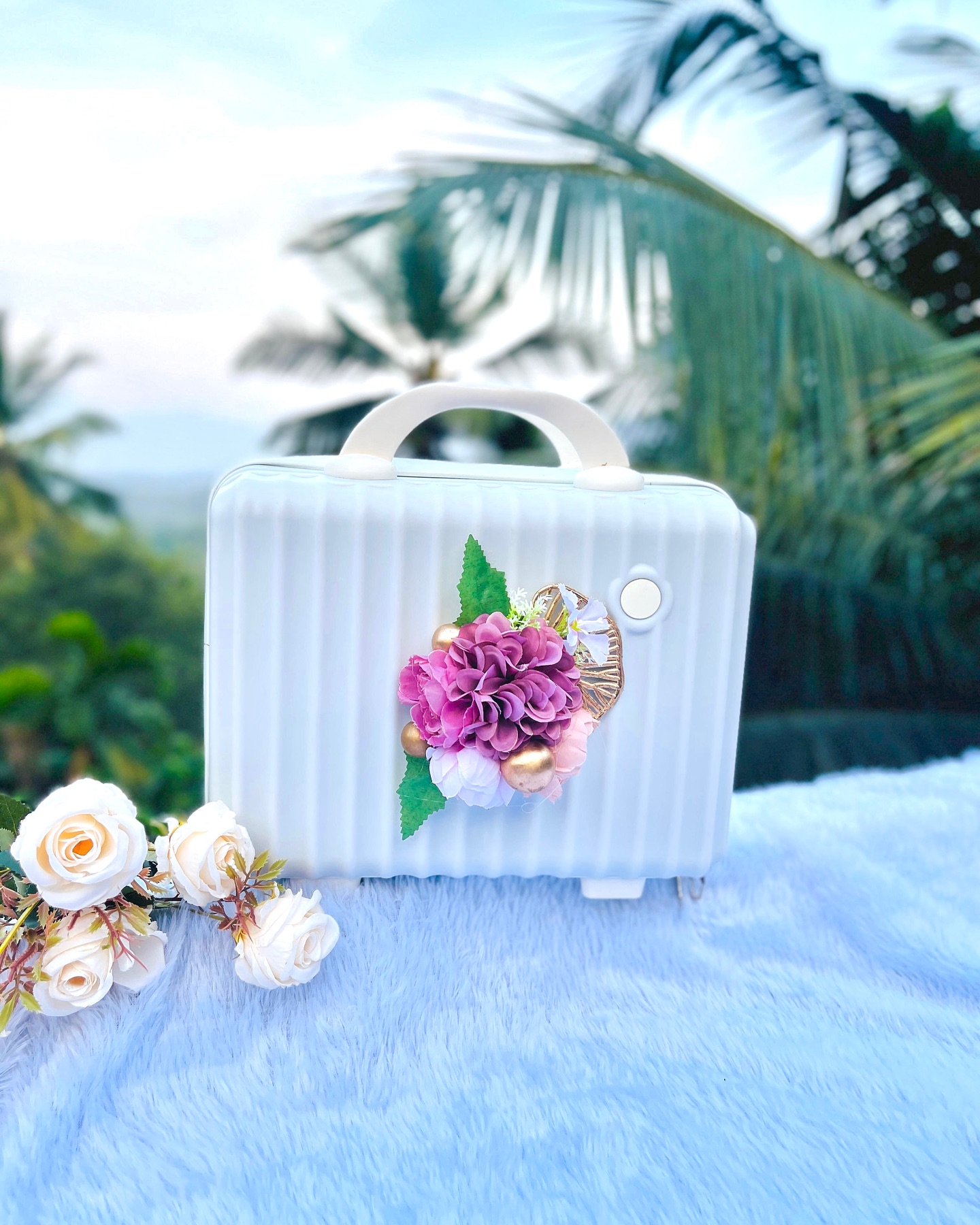 A charming white mini suitcase-shaped box decorated with a pink and mauve floral arrangement and gold accents.