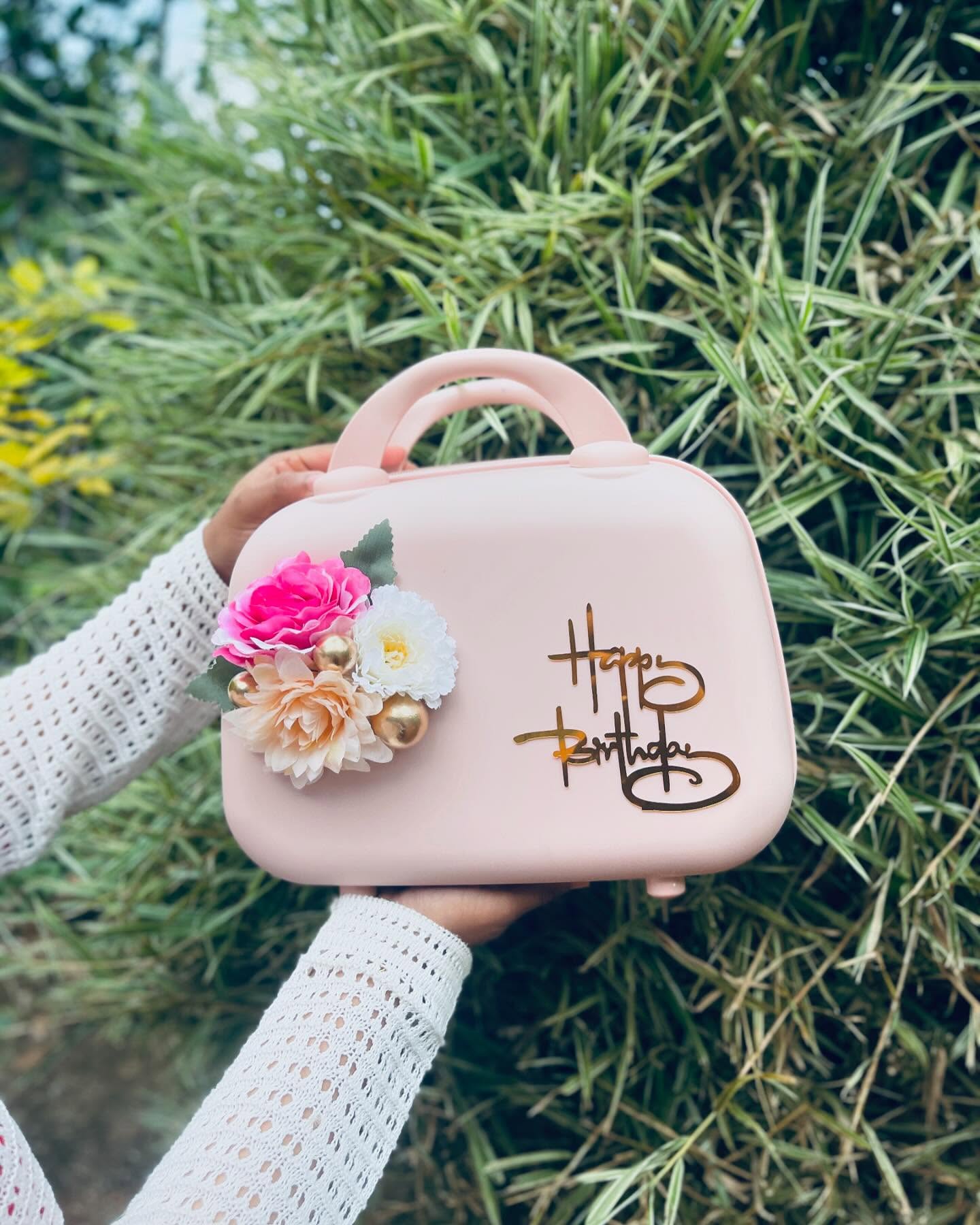 A blush pink vanity case adorned with a rose corsage and gold "Happy Birthday" script.