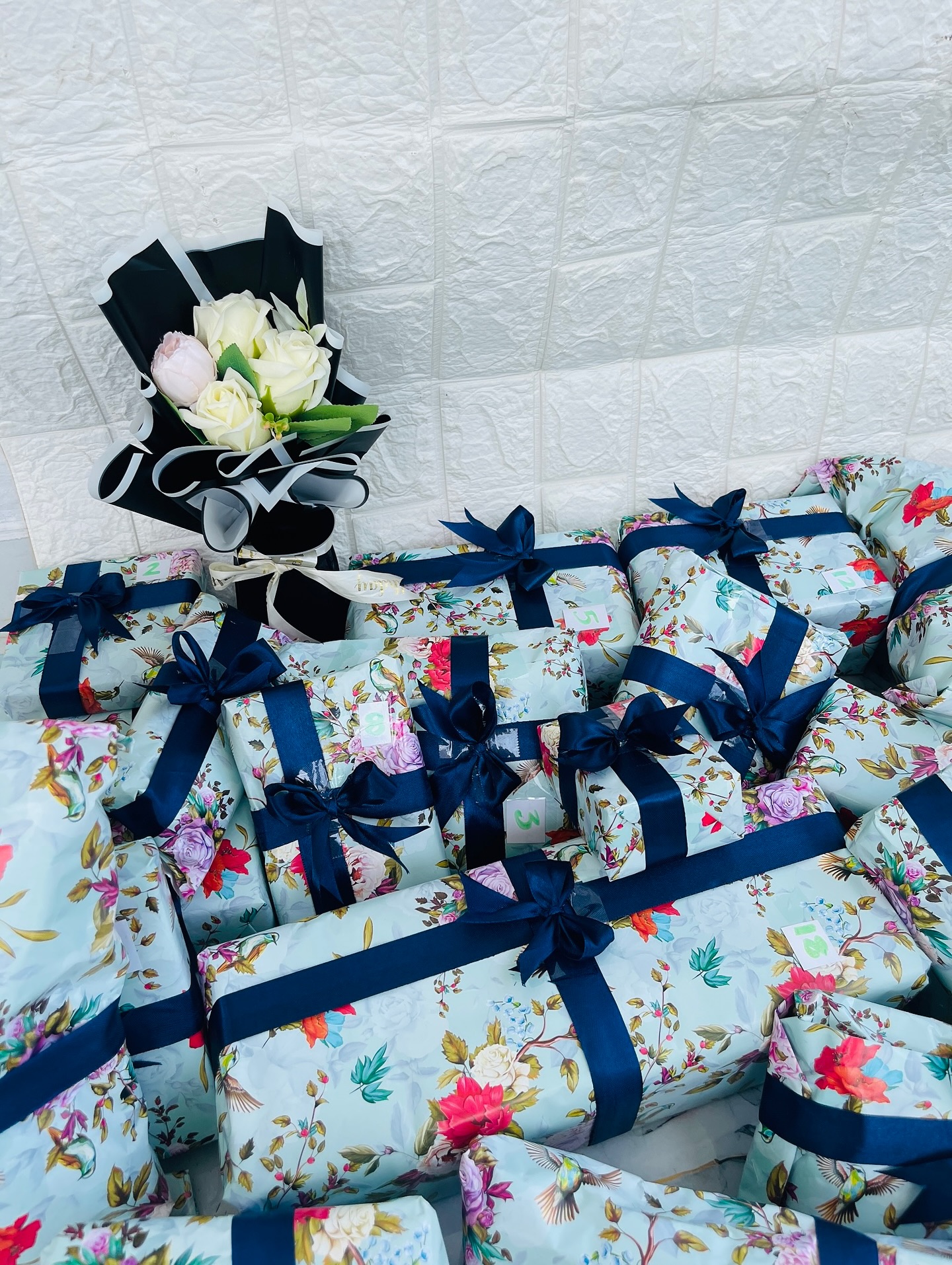 A numbered bulk set of gift boxes wrapped in matching vintage floral paper with navy ribbon bows, alongside a small bouquet.