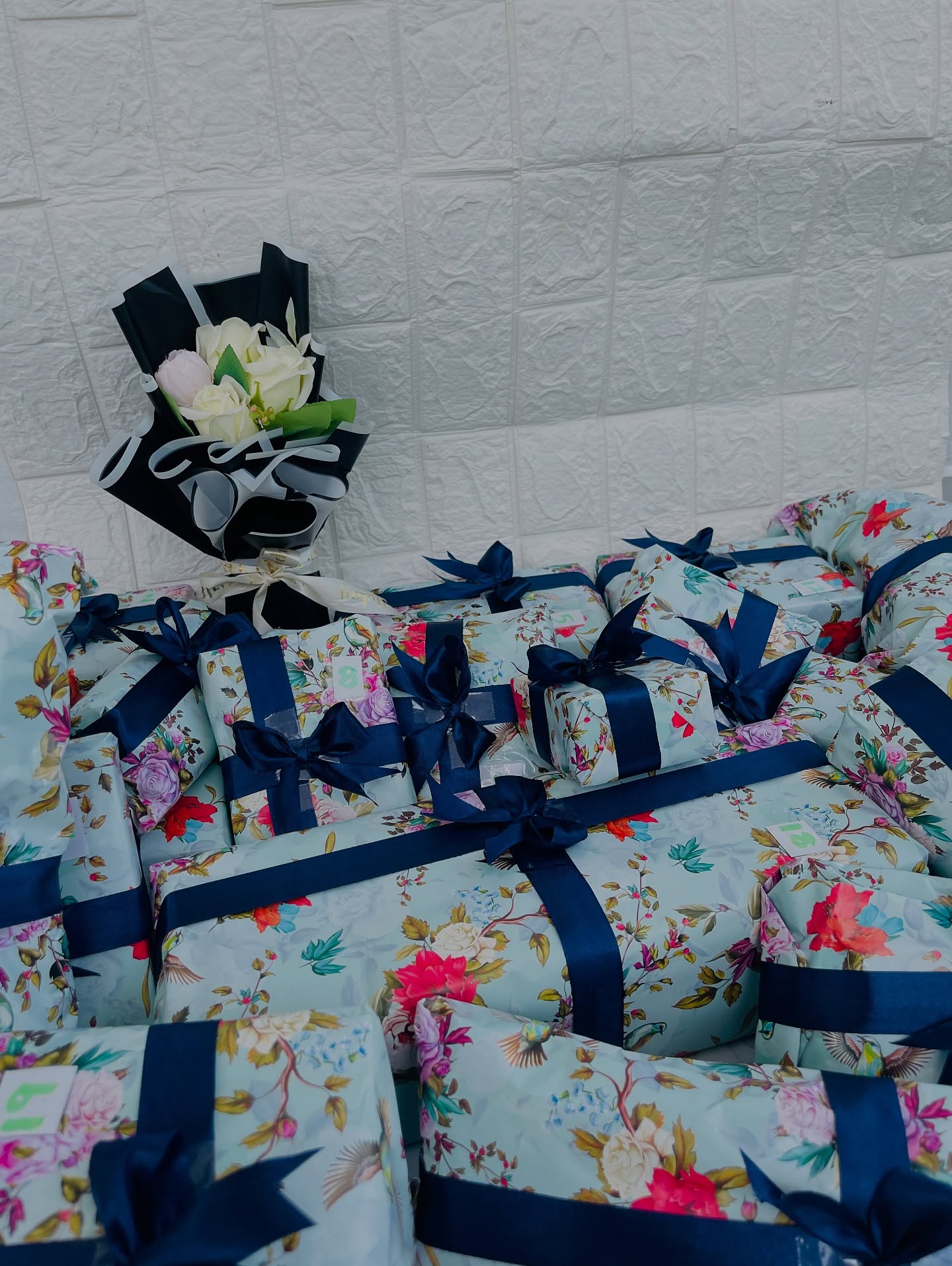 A set of numbered floral-wrapped favour boxes with navy ribbon bows and a matching mini bouquet.