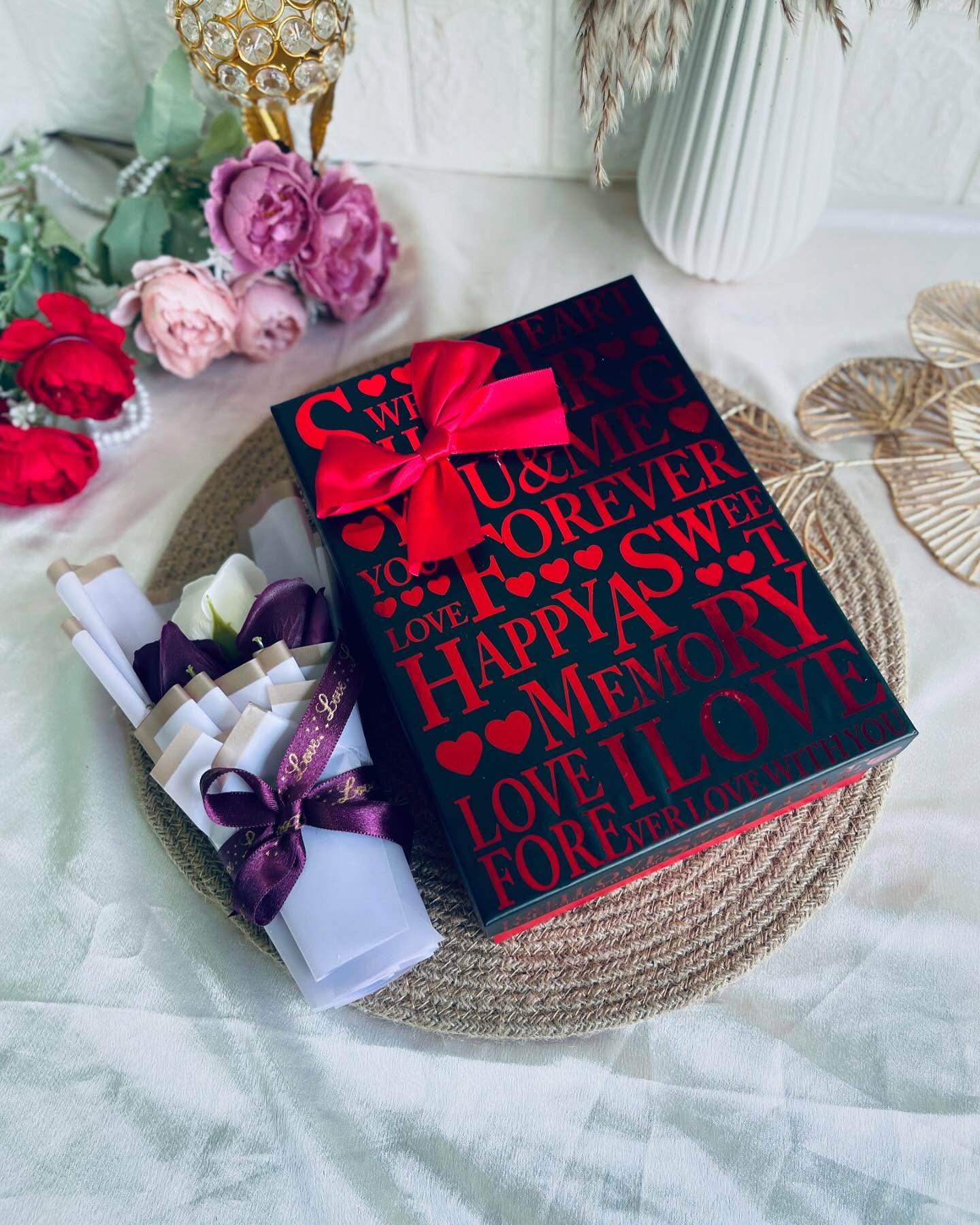 A bold black and red anniversary keepsake box topped with a satin bow and rolled love-note scrolls.