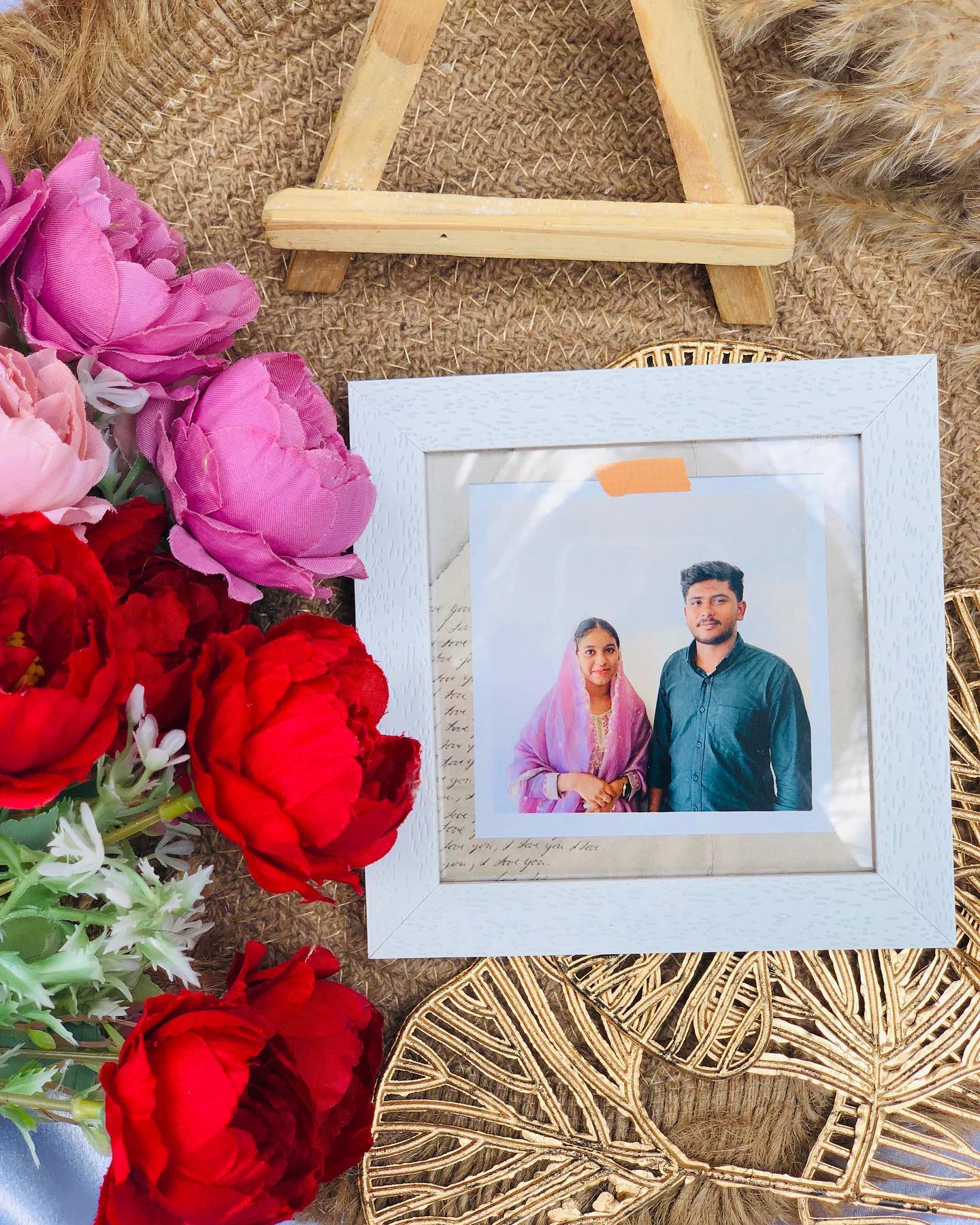 A custom-printed couple photo in a whitewashed frame, displayed on a mini wooden easel with red and pink roses.