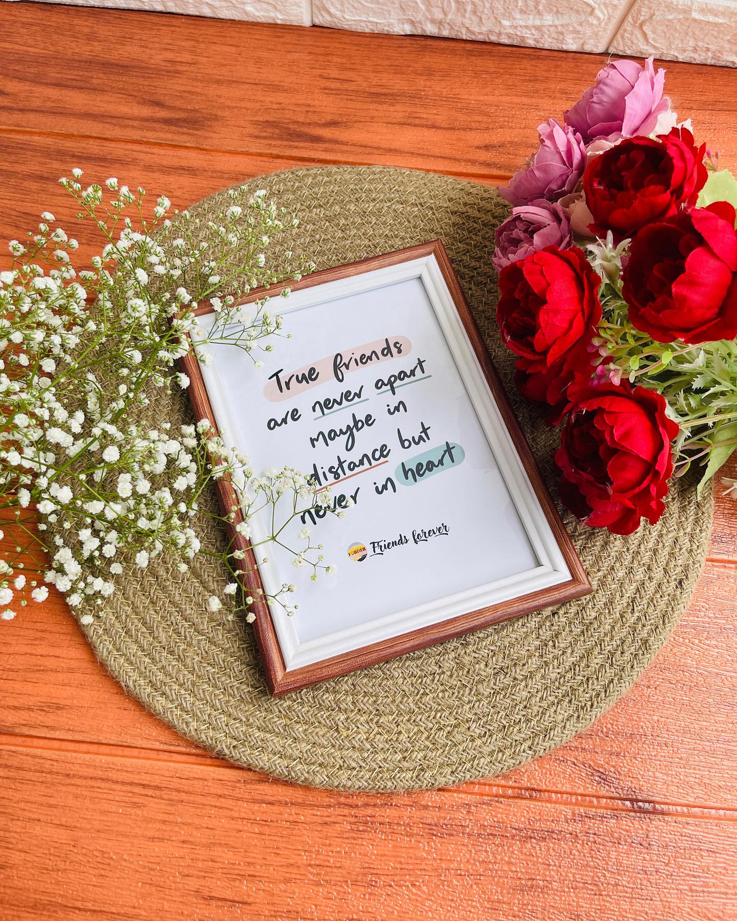 A heartfelt 'Friends Forever' quote frame set beside a bouquet of red and mauve roses with baby's breath.