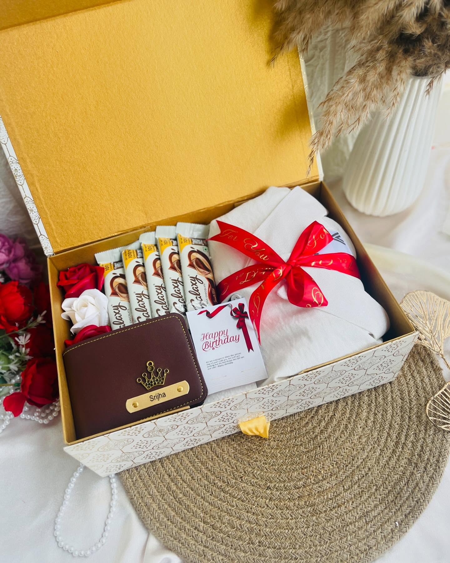 A golden birthday box loaded with Galaxy chocolate bars, a name-engraved wallet, roses, and a wrapped surprise.