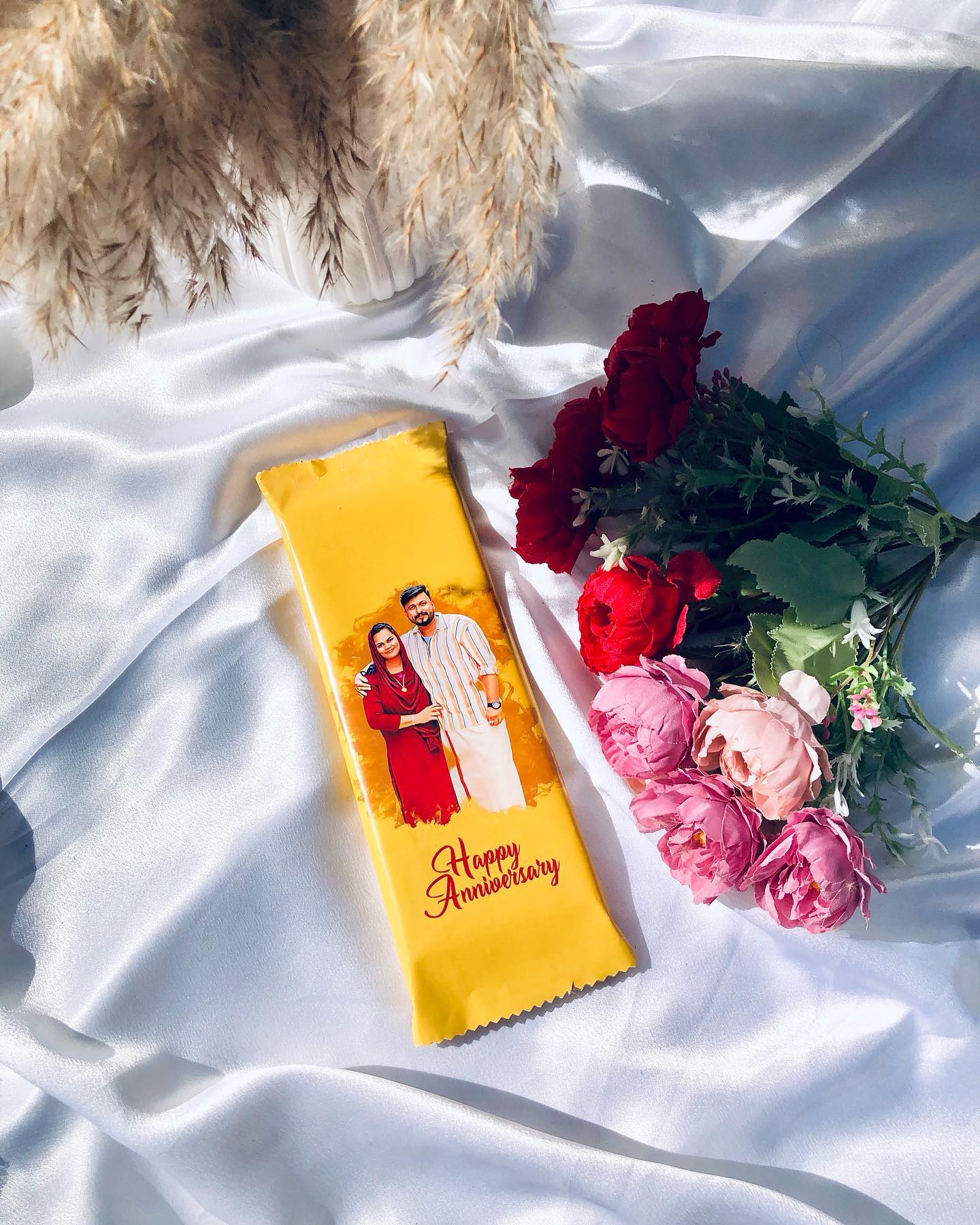 A jumbo chocolate bar personalized with a couple's photo and a "Happy Anniversary" print, paired with a red rose bouquet.