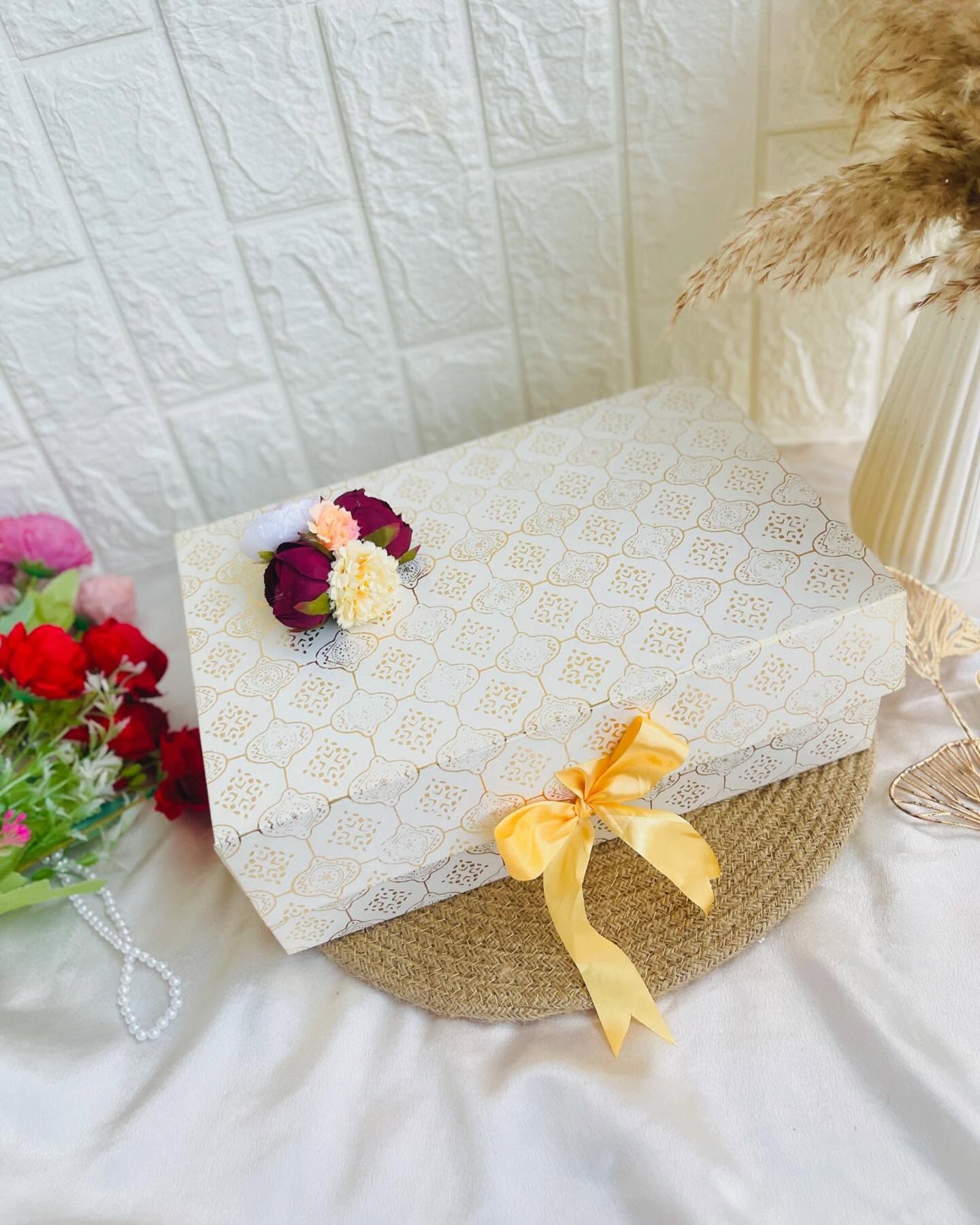 A quatrefoil-patterned gift box tied with a sunny yellow ribbon and topped with a delicate flower cluster.