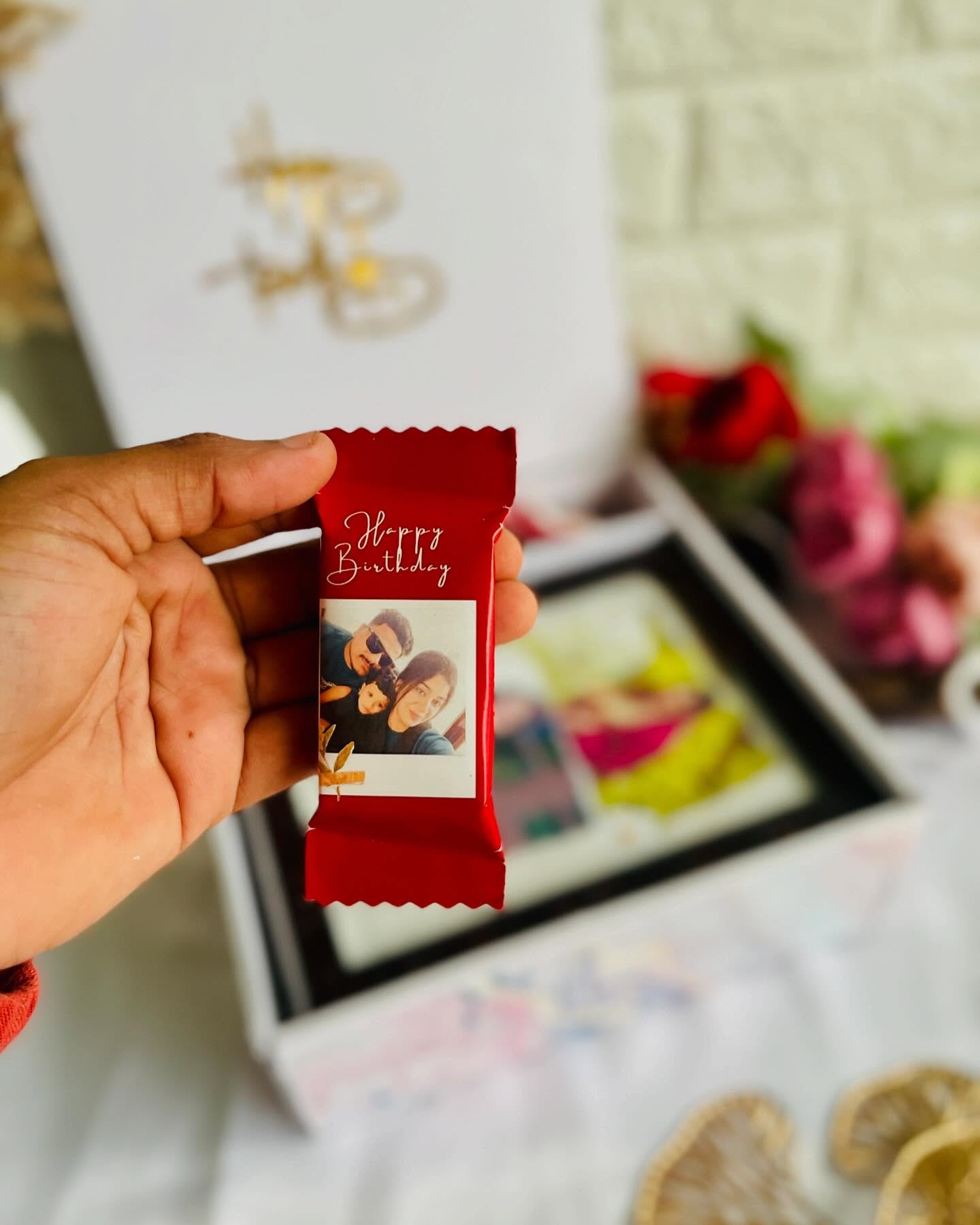 An opened marble-finish gift box featuring a personalized photo frame, chocolates, and a gold 'Happy Birthday' topper.