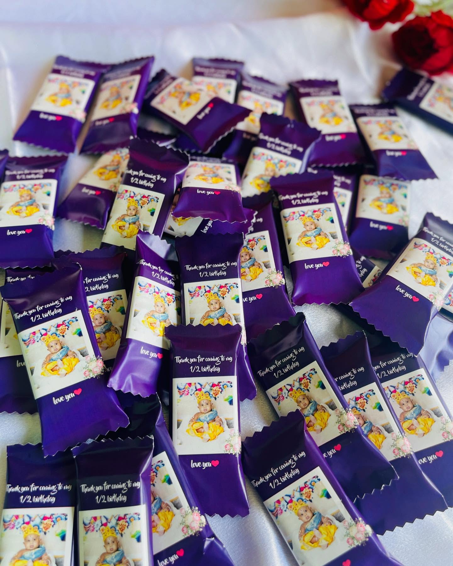 Purple-wrapped mini chocolate bars personalized with a baby's photo and a 'Thank you for coming to my 1/2 birthday' message.