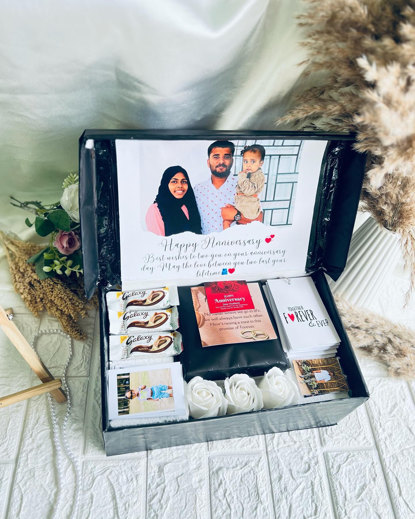 An open keepsake box with a printed family photo, Galaxy chocolates, love notes, and soft roses.