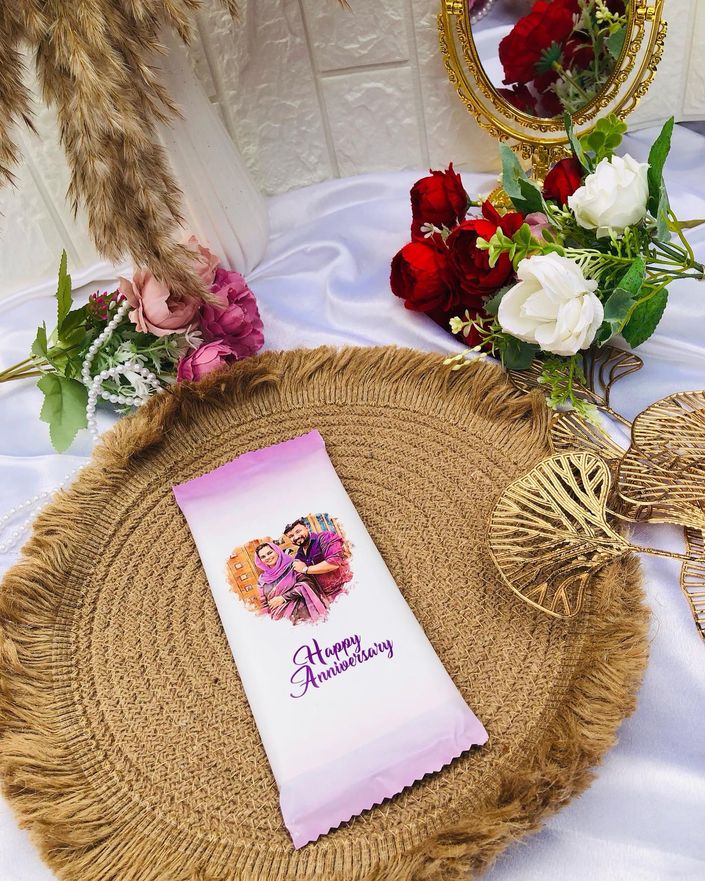 A personalized chocolate bar printed with a couple's photo and a Happy Anniversary message, styled among fresh roses.