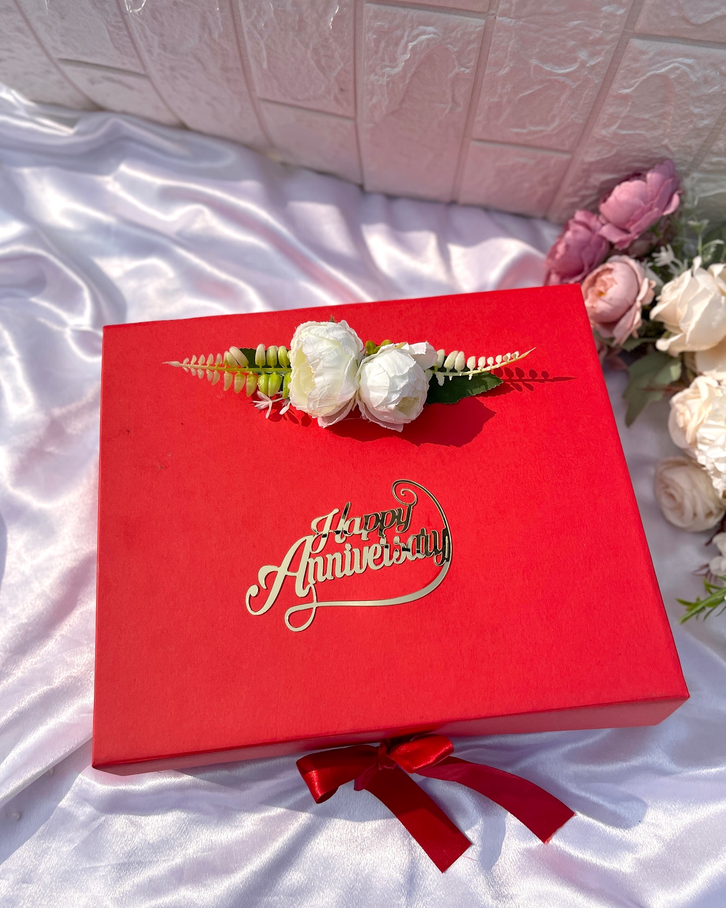 An elegant red gift box finished with a floral topper and gold 'Happy Anniversary' script, ready to be filled with treats for the couple.