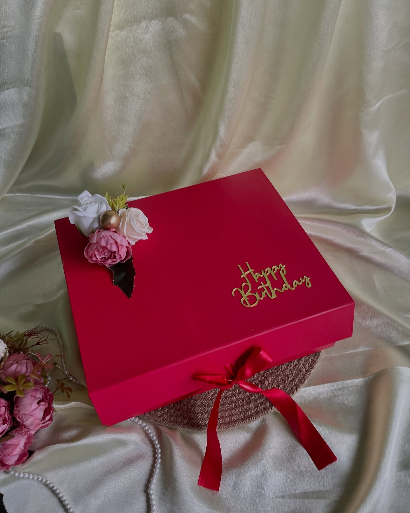 A magenta gift box topped with pastel roses and a gold 'Happy Birthday' script, tied with a satin ribbon.
